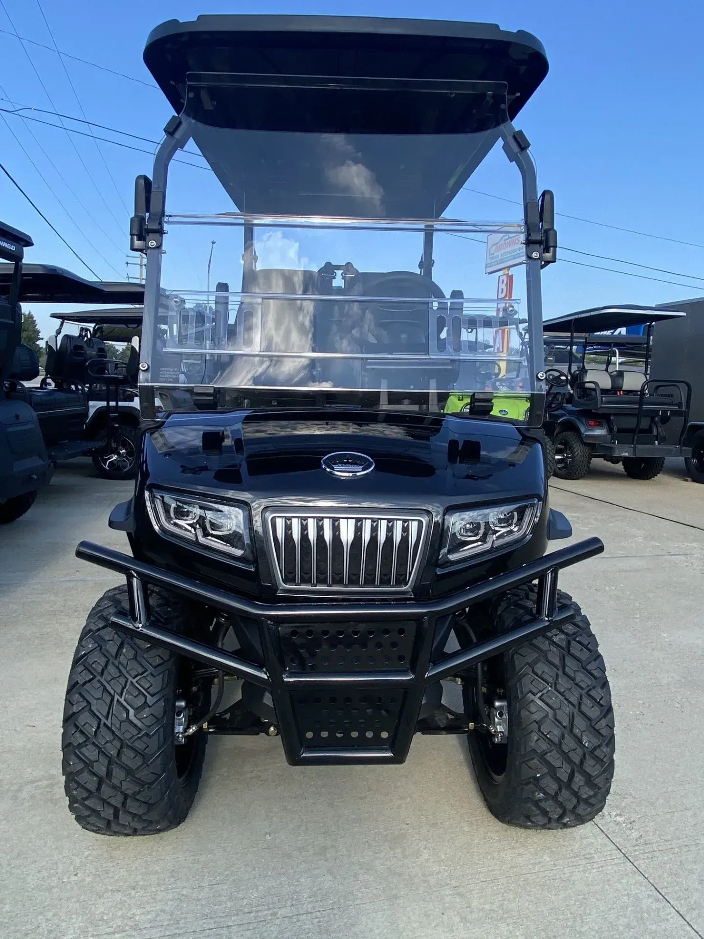 Black golf cart with front bumper and off-road tires, parked on pavement.