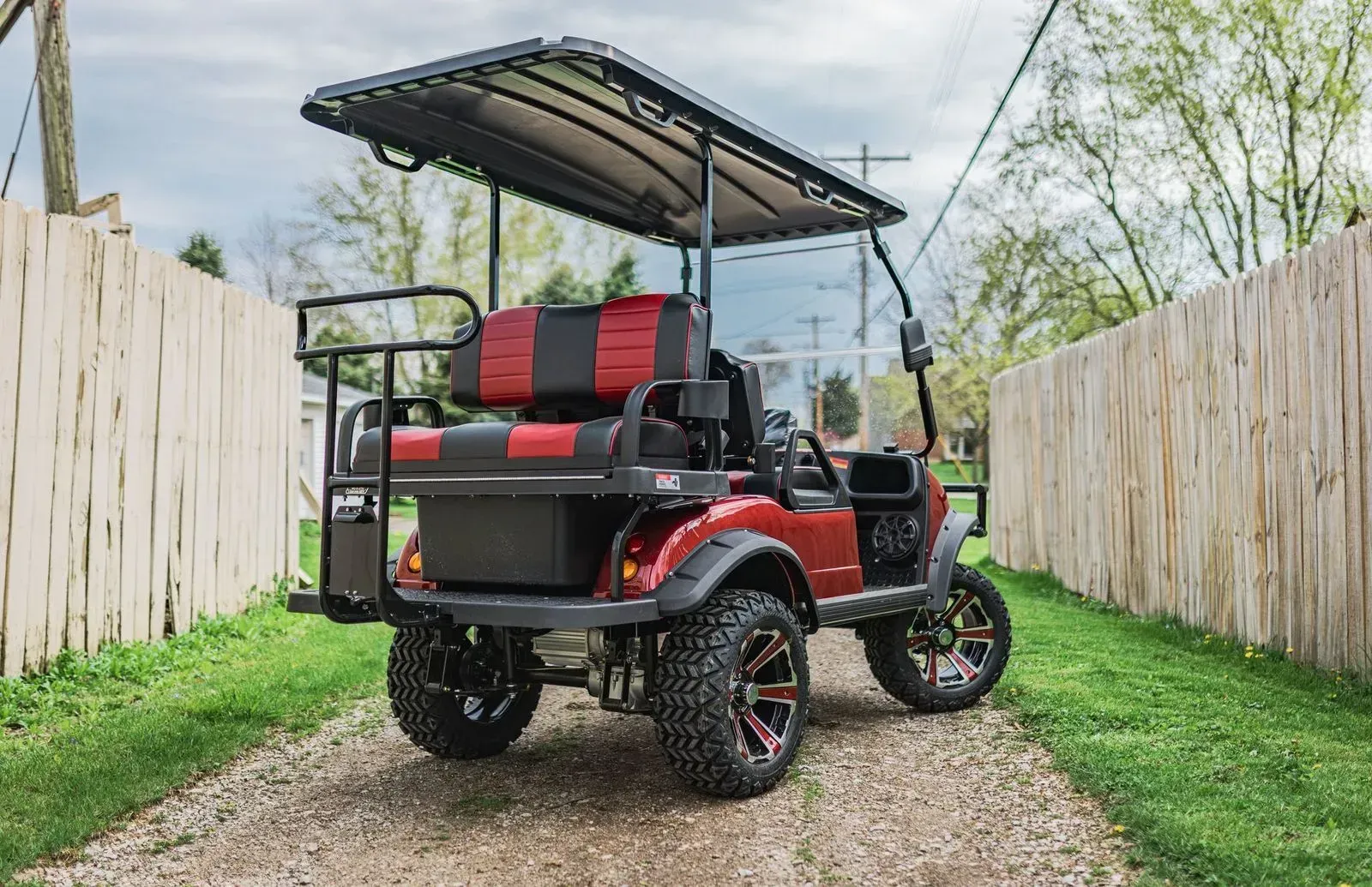 Red golf cart with black accents, large tires, and canopy, parked on gravel path.