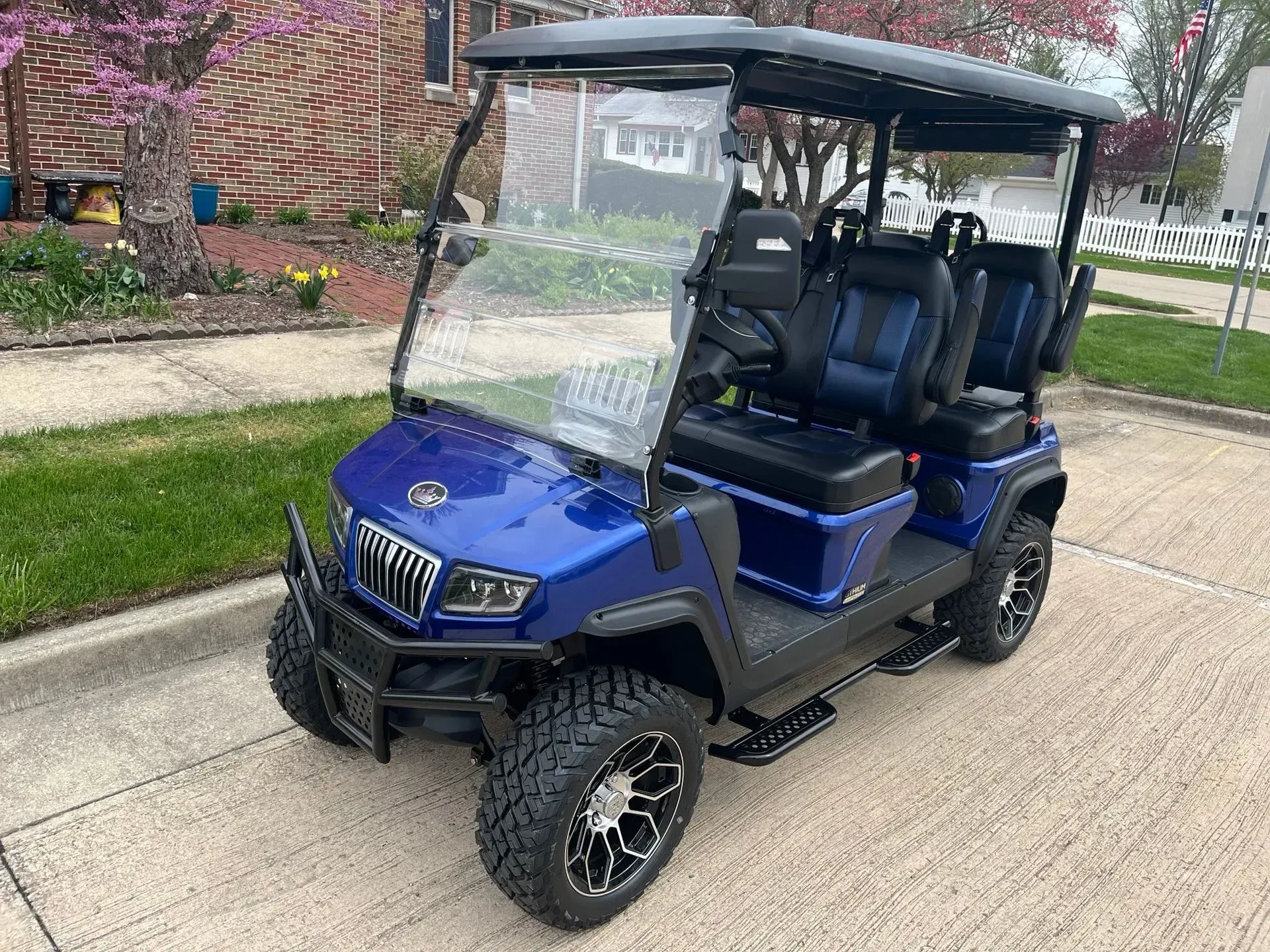 Blue golf cart with black accents, six seats, and off-road tires parked on a paved surface.