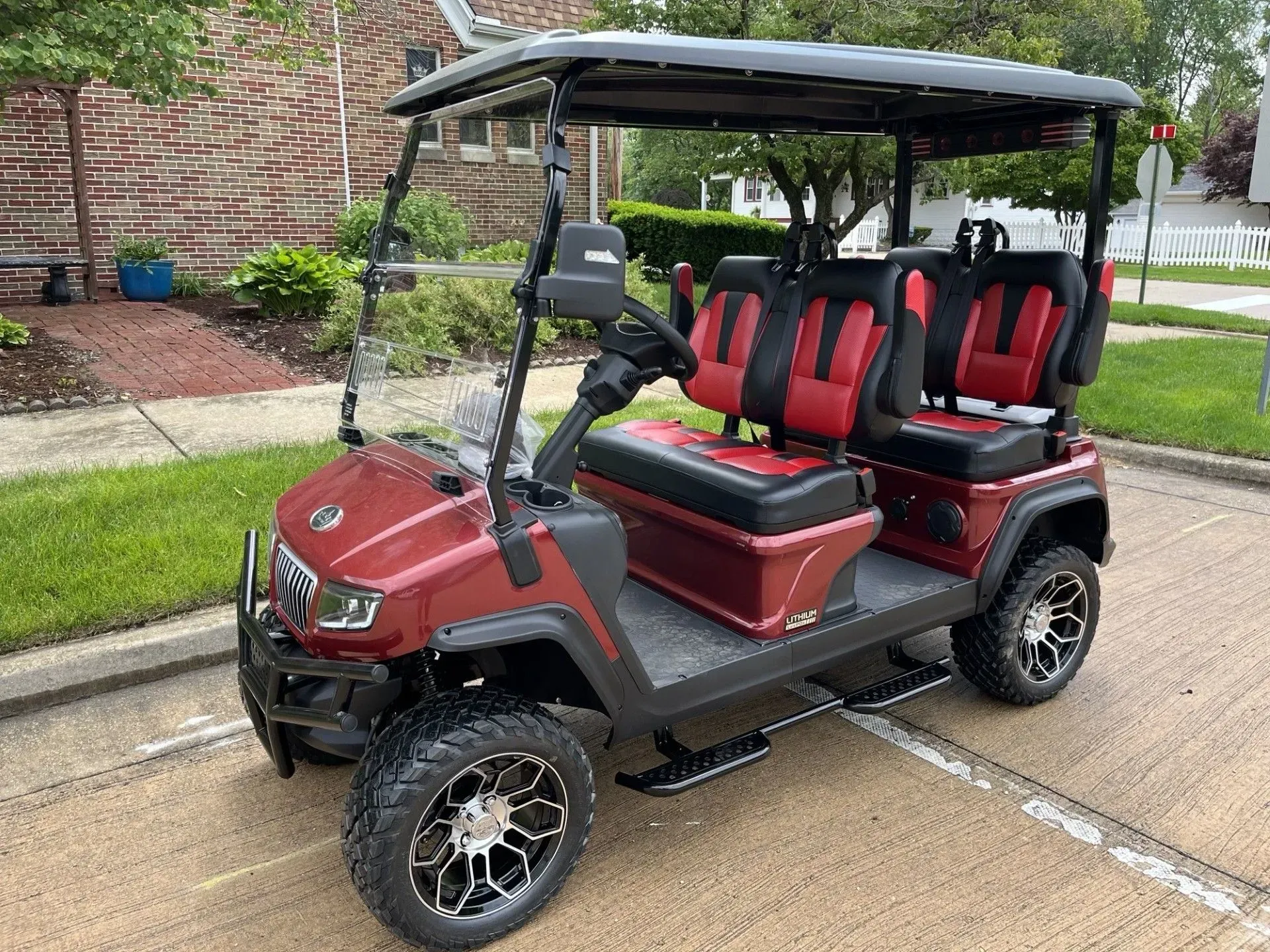 Red and black golf cart on a street, four seats, black roof, and large tires.