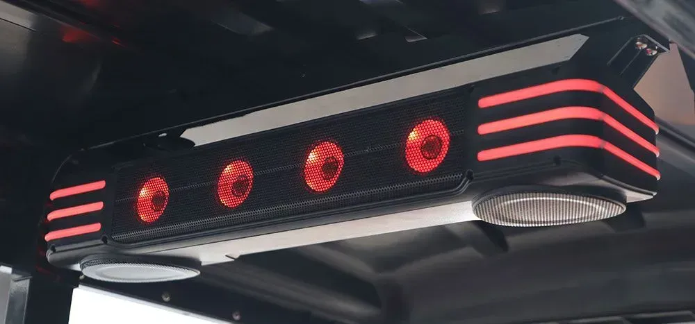 Black speaker with red lights and a reflective metal surface, mounted on a dark surface.