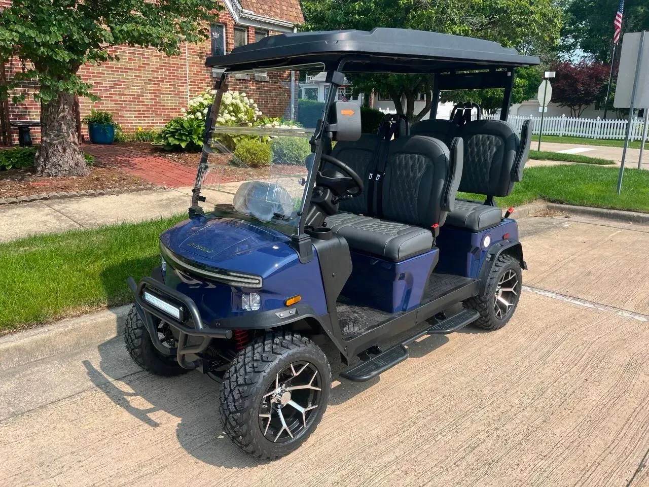 Blue golf cart with black roof parked on pavement, facing the camera.