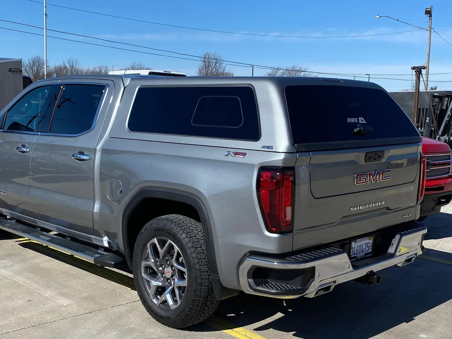 Gray GMC truck with a black cap, parked outside on a sunny day.