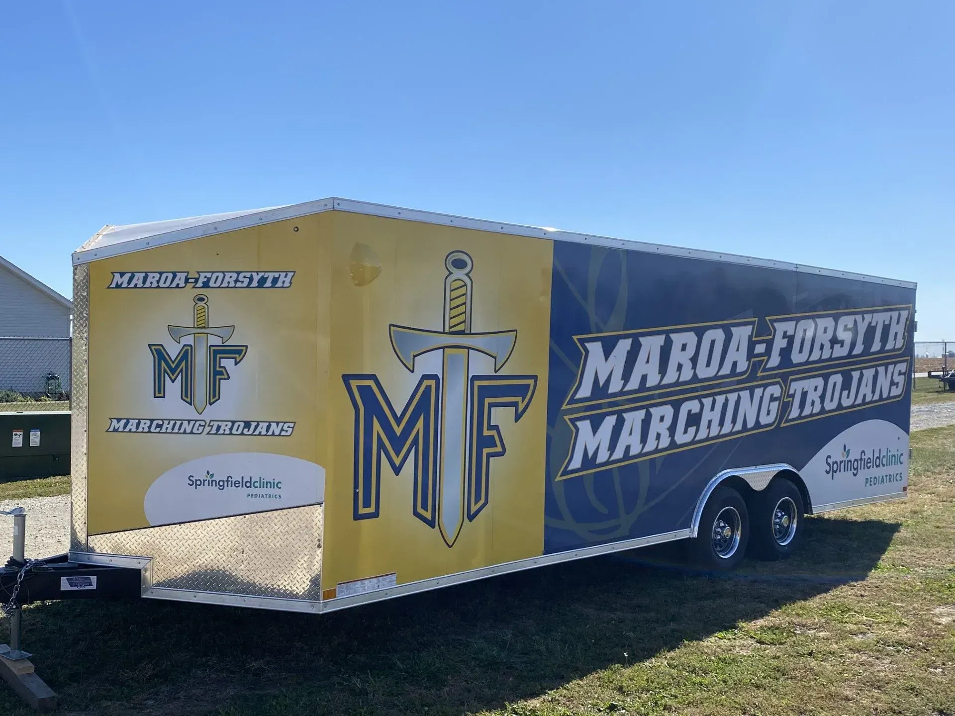 Trailer with Maroa-Forsyth Marching Trojans logo in yellow and blue.