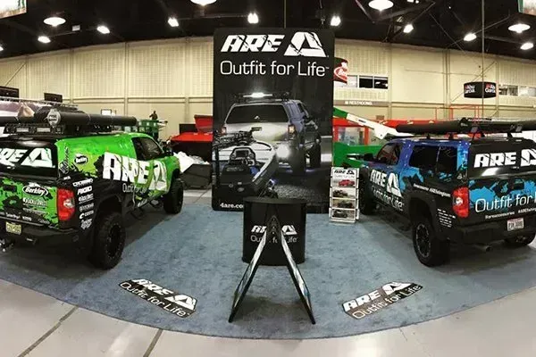 ARE truck display booth featuring green and blue trucks. Black sign and flooring.