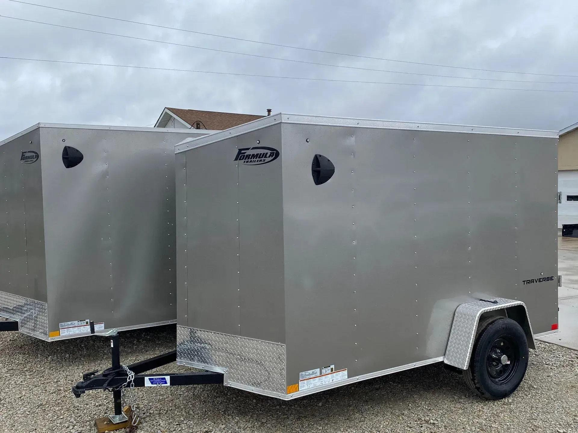 Two silver enclosed cargo trailers parked on gravel.