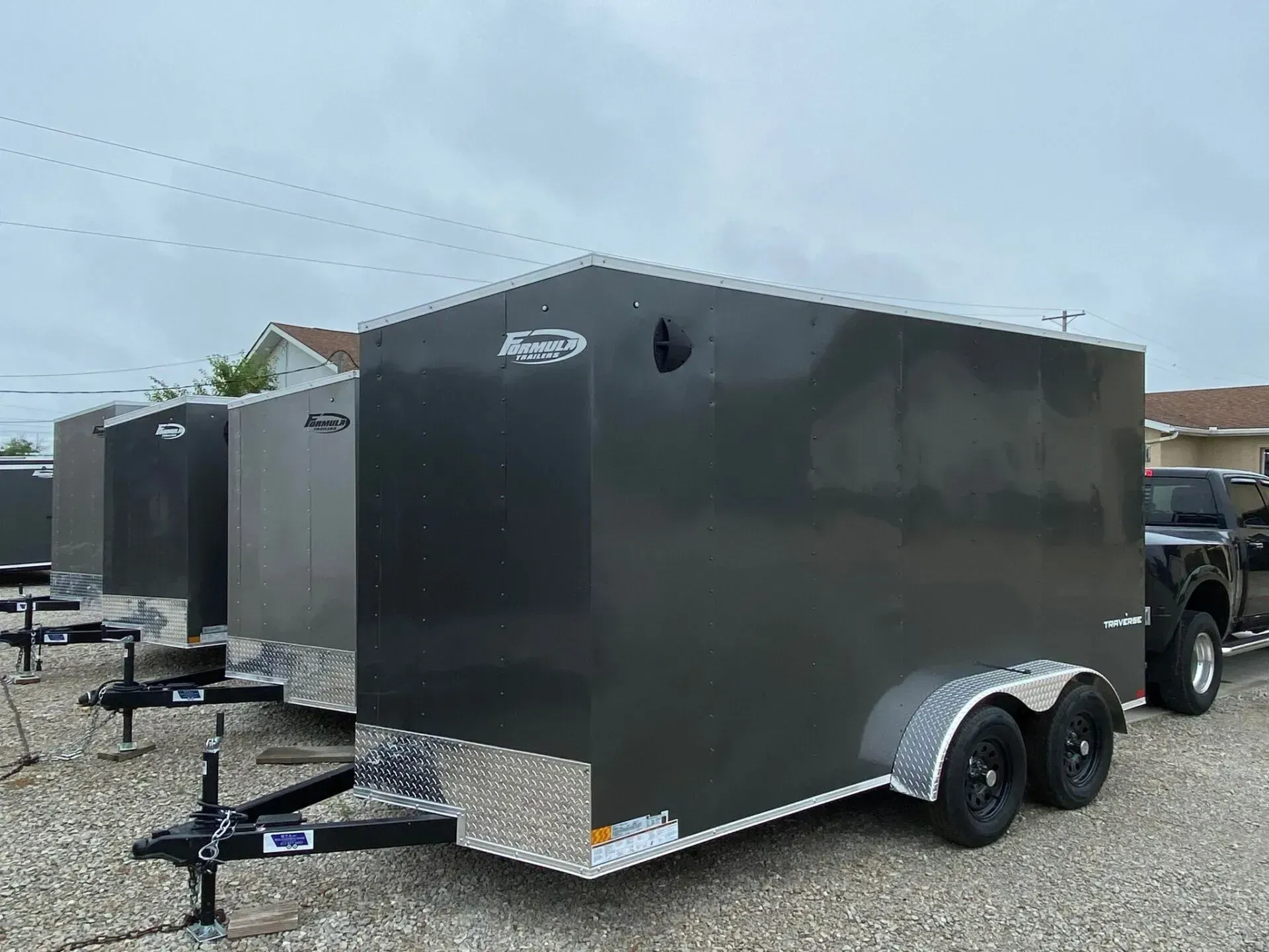 Several dark gray enclosed cargo trailers parked outside, with a truck visible.
