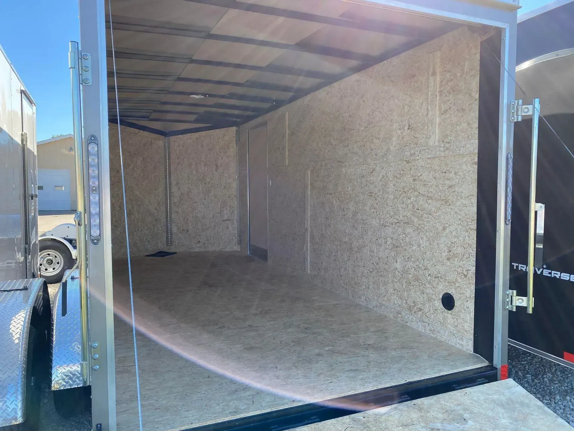 Empty cargo trailer interior, wood walls and floor, open rear door.