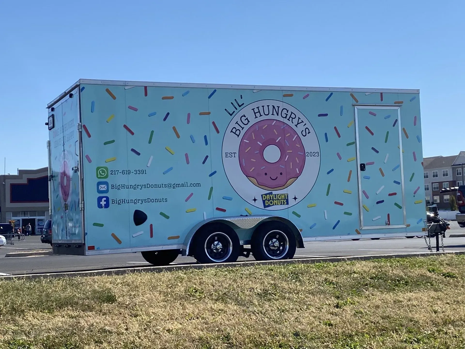 Food truck with a light blue sprinkle design and a donut logo, parked outdoors.
