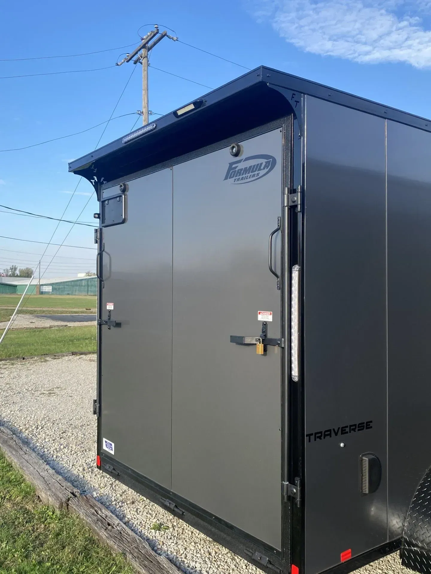 Gray enclosed trailer with black trim and door handles against a sky with power lines.