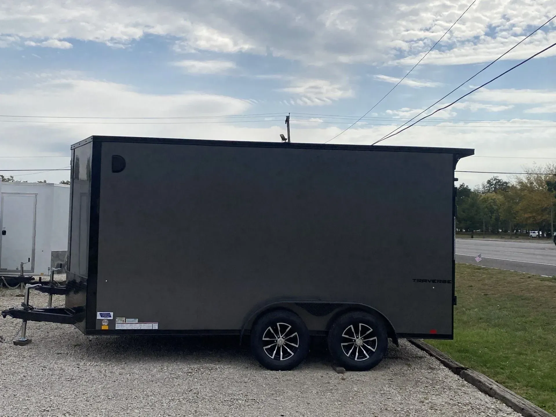 Dark gray enclosed cargo trailer parked on gravel, with dual wheels and a sky background.