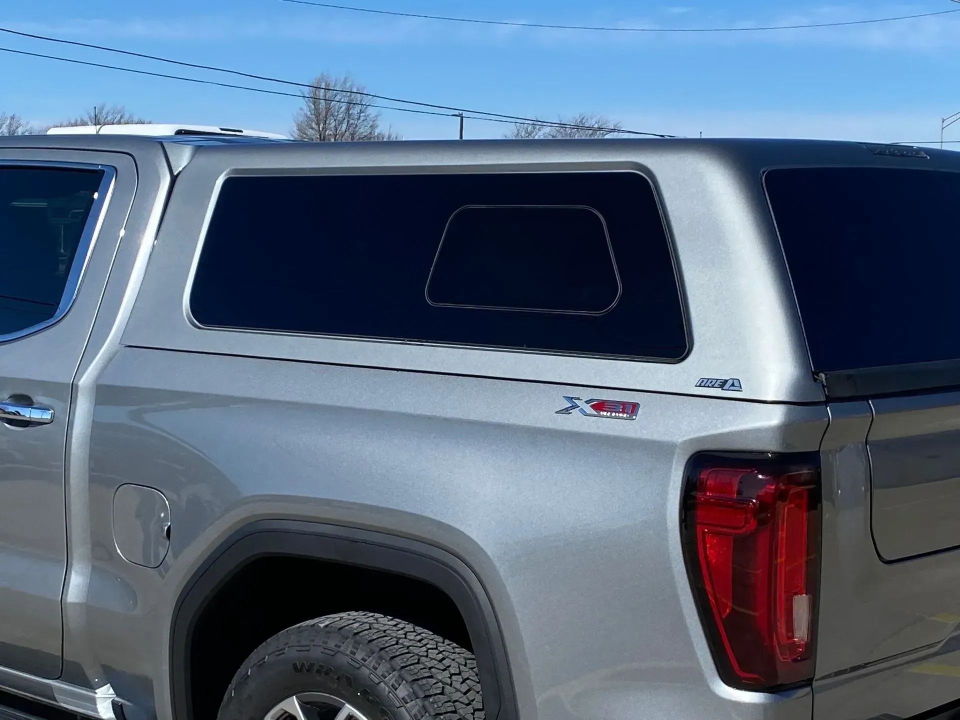 Silver pickup truck with a silver camper shell, tinted windows.