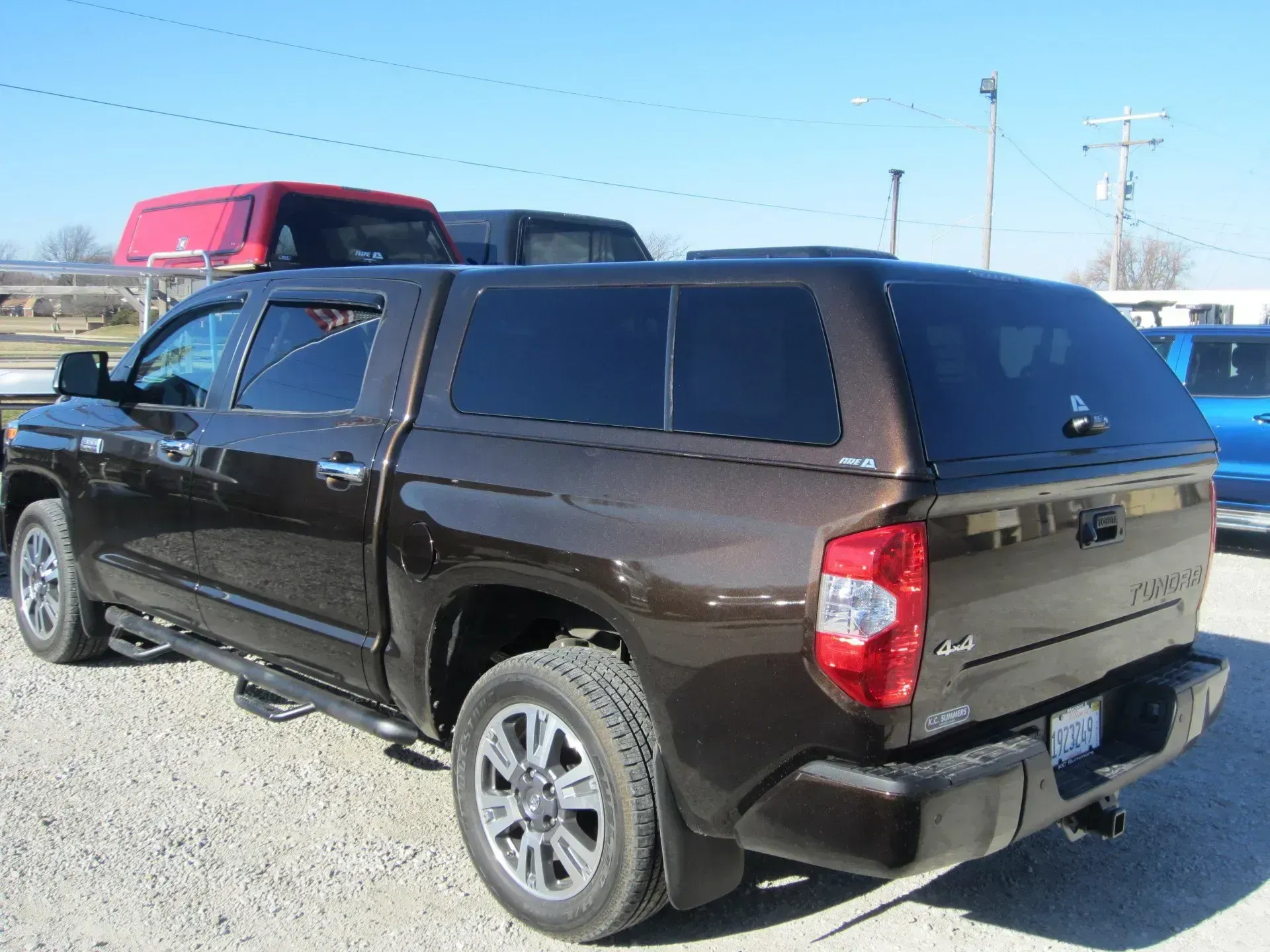 Brown Toyota Tundra pickup truck with a matching camper shell parked outdoors on a sunny day.
