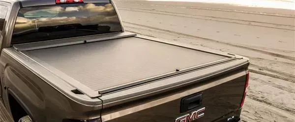 A brown GMC truck on a beach with a closed black tonneau cover.