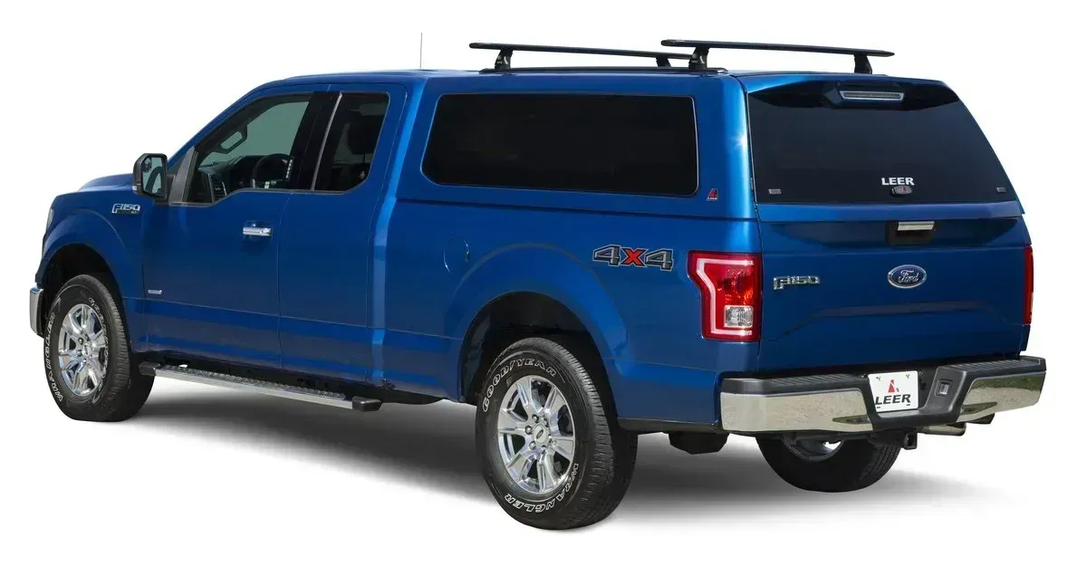 Blue Ford F-150 truck with a camper shell and roof rack, parked outdoors.