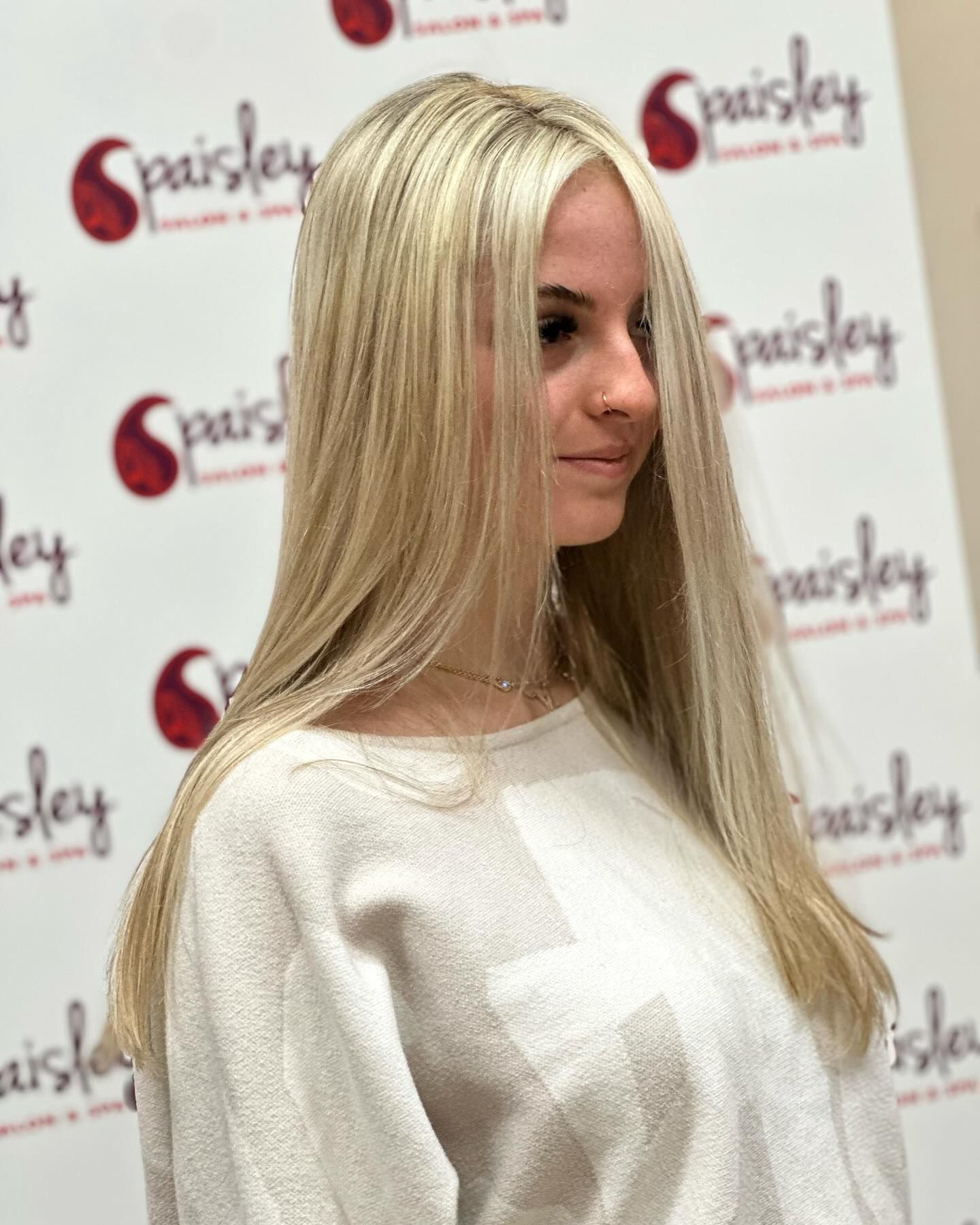 A woman with long blonde hair is wearing a white sweater.