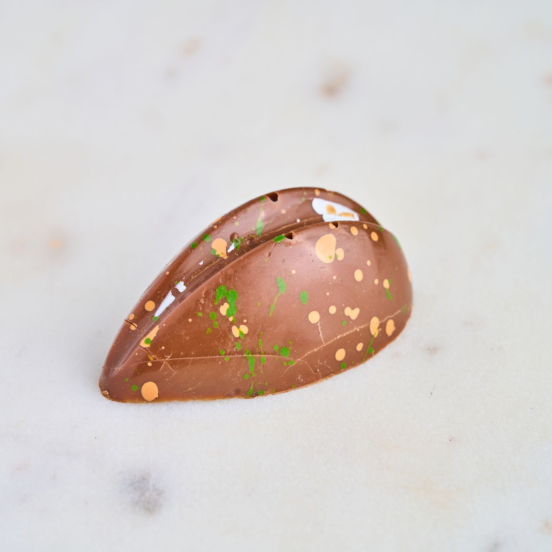 Chocolate truffle with brown, gold, and green splatter on a marble surface.
