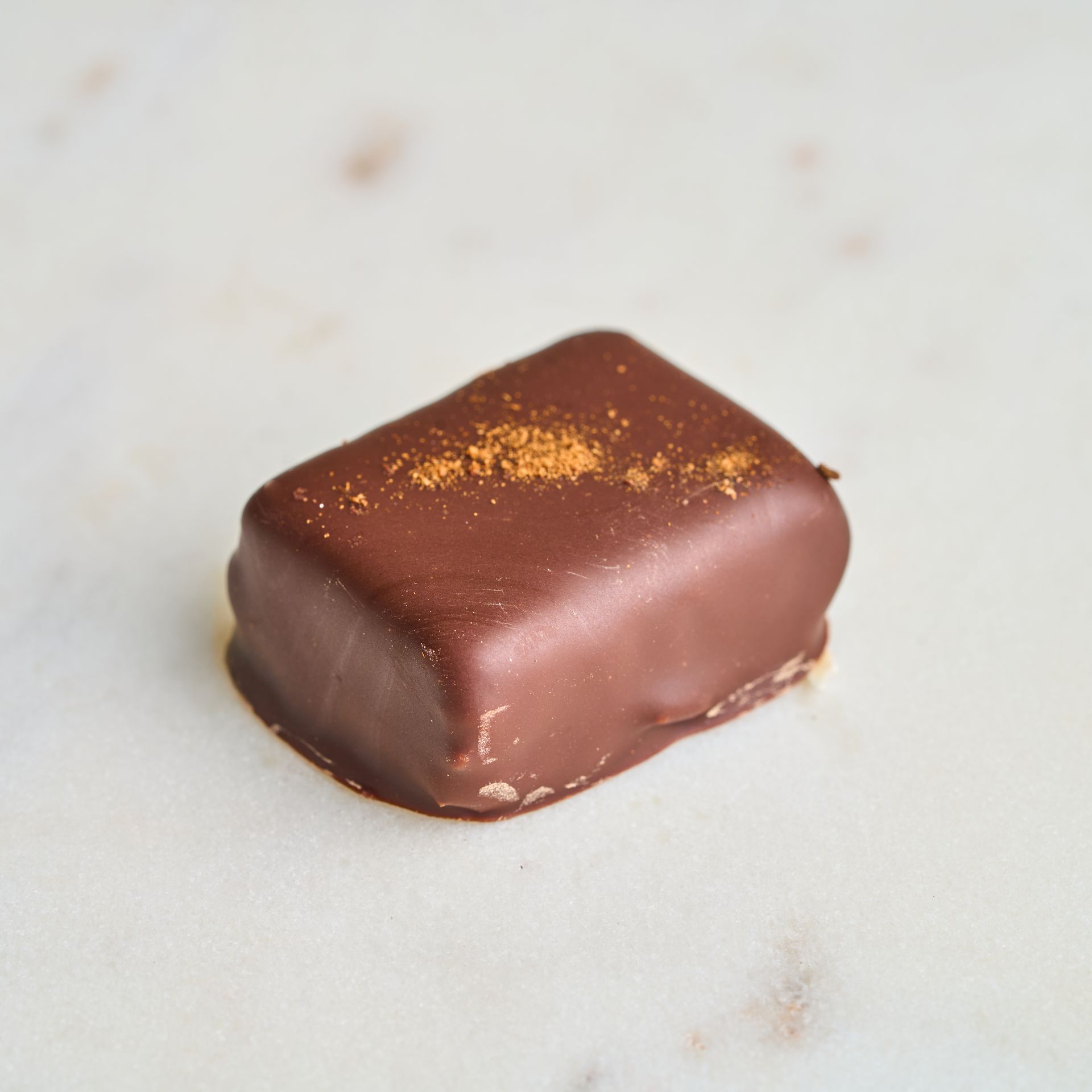 Chocolate candy, rectangular, with cinnamon sprinkle on top, on a white surface.