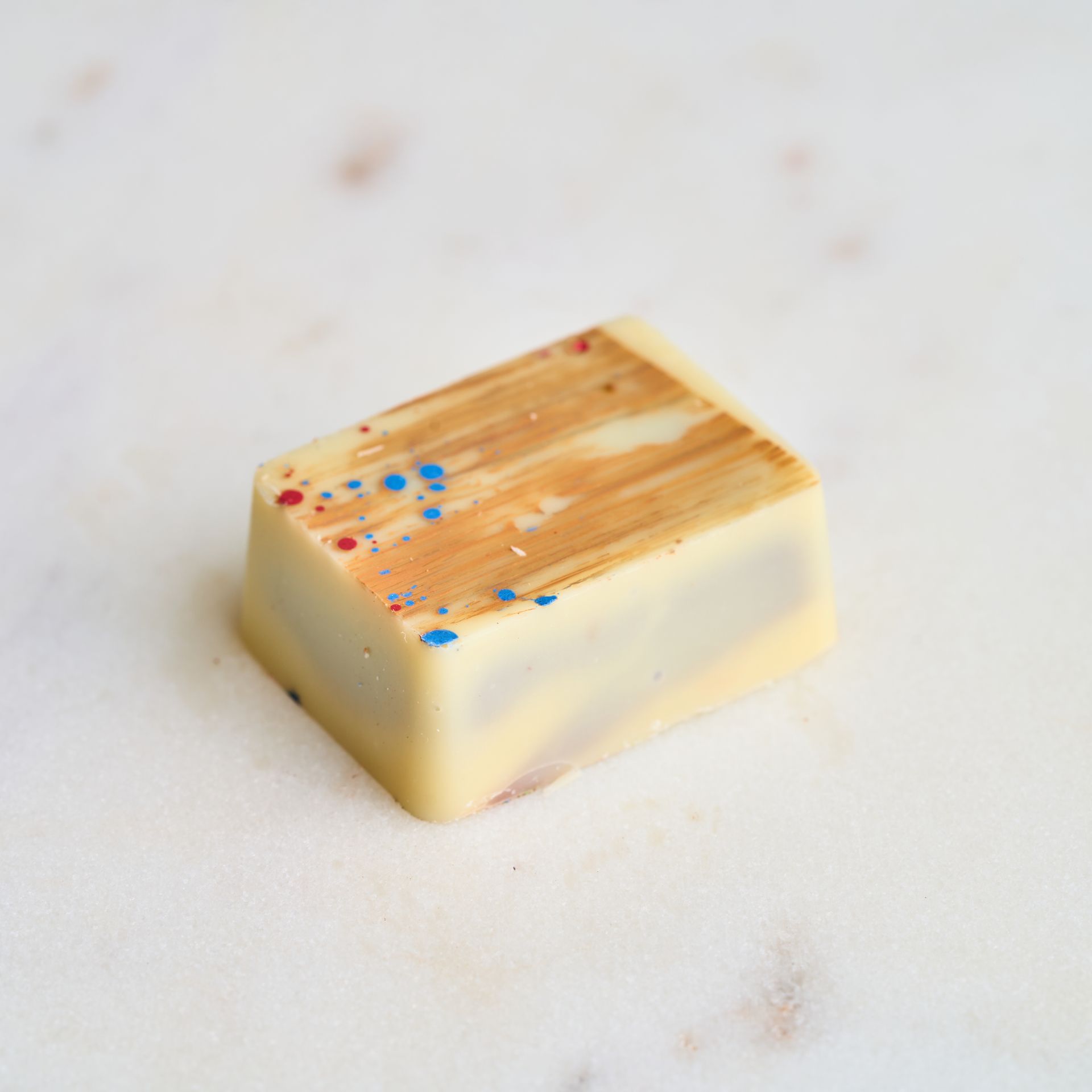 White chocolate confection with gold-brown strokes and red/blue speckles, set on a marble surface.