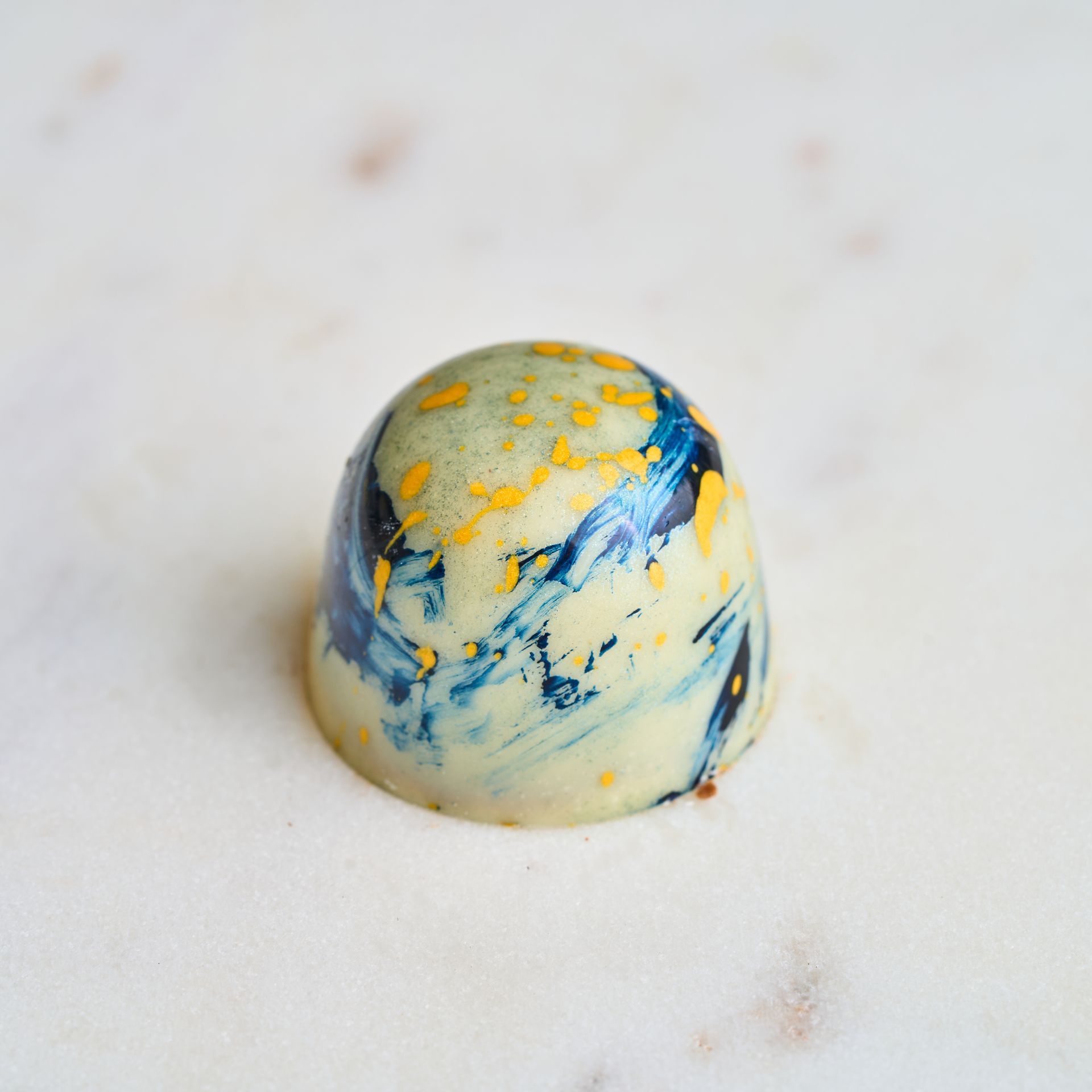 Chocolate truffle with marbled blue, white, and gold design on a white surface.