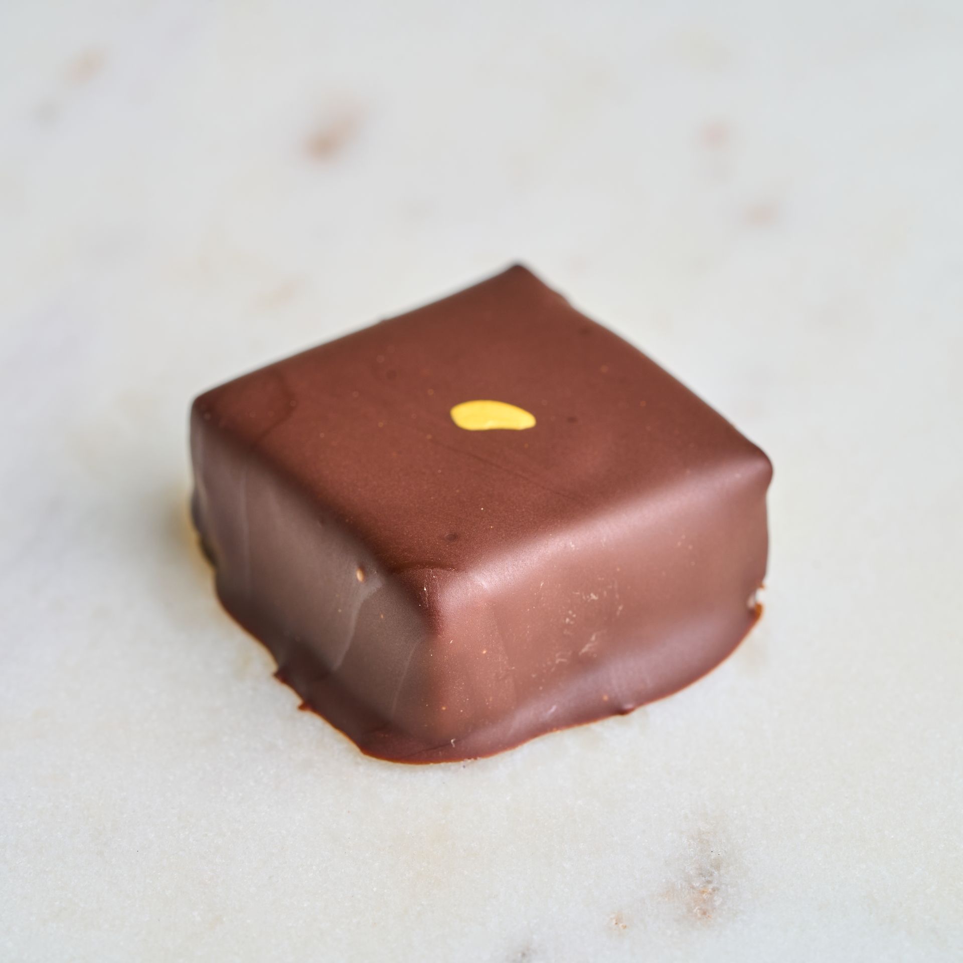 Square chocolate candy with a gold accent on a marble surface.