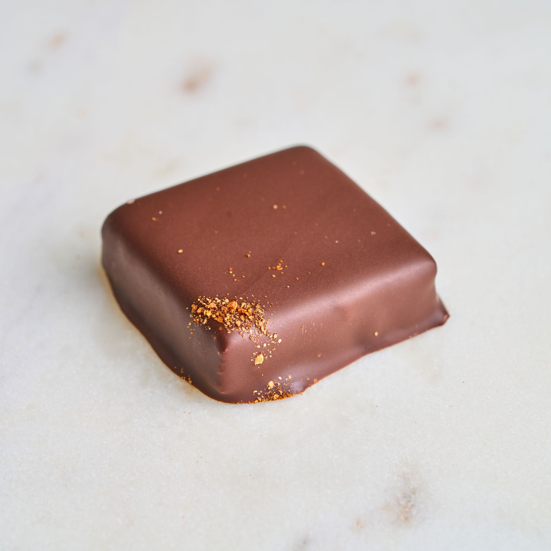 Square chocolate candy with gold dust on a marble surface.