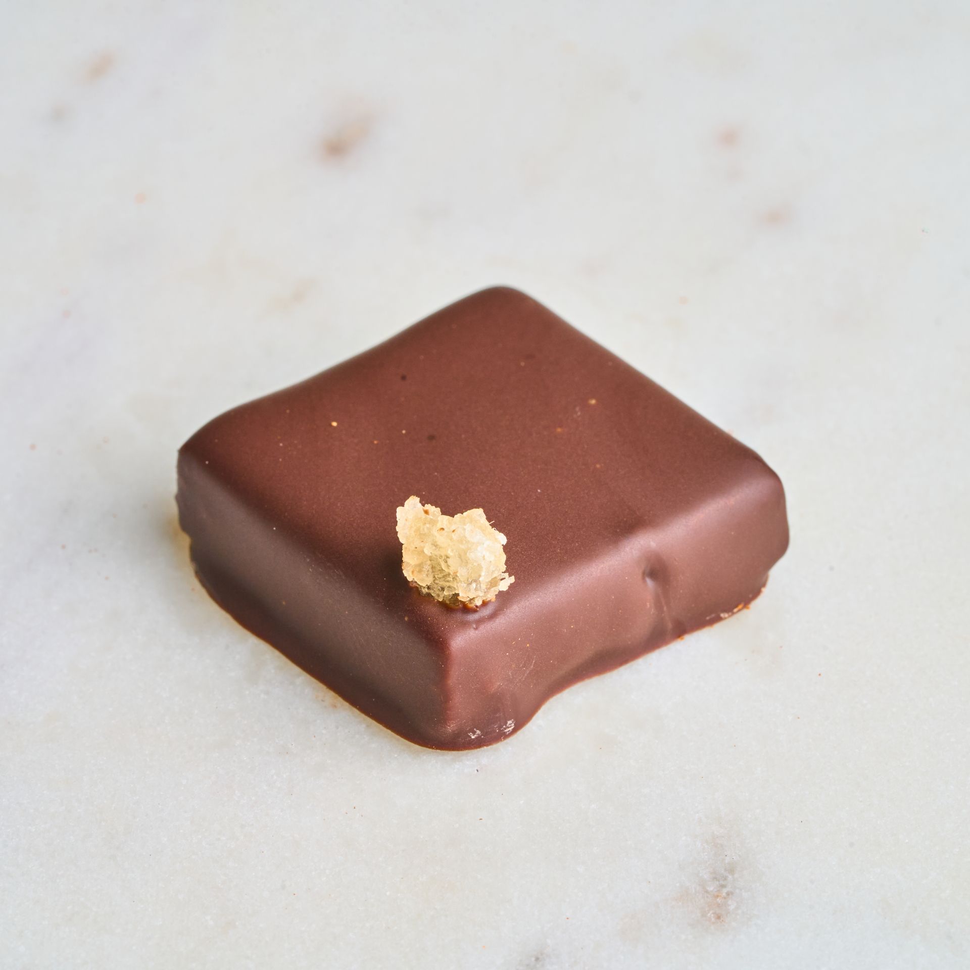 Chocolate square with gold garnish on a marble surface.