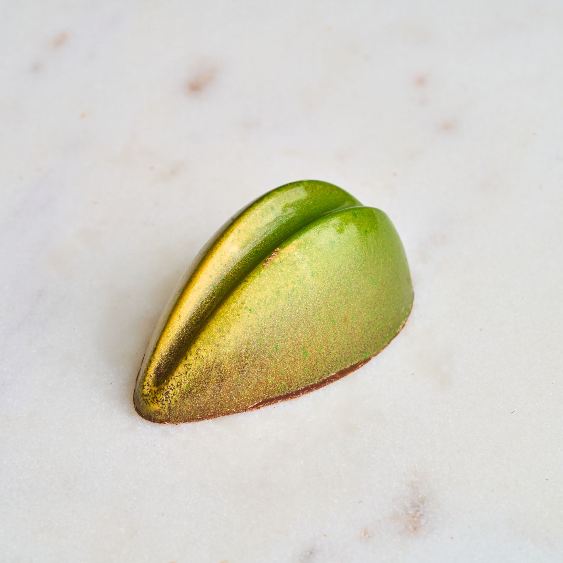 Green and gold chocolate candy, leaf-shaped, on a white marble surface.