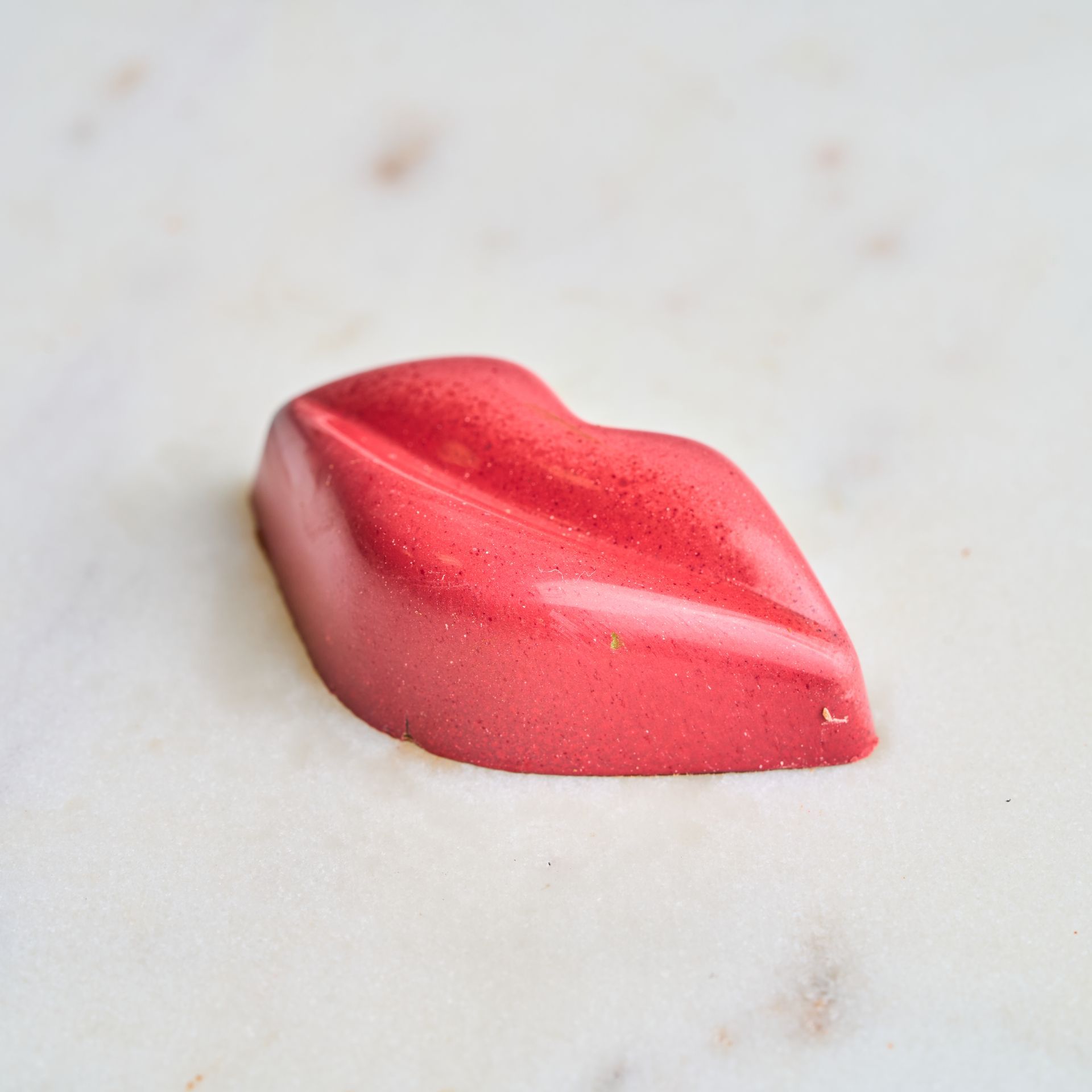 Pink chocolate candy in the shape of lips on a white marble surface.