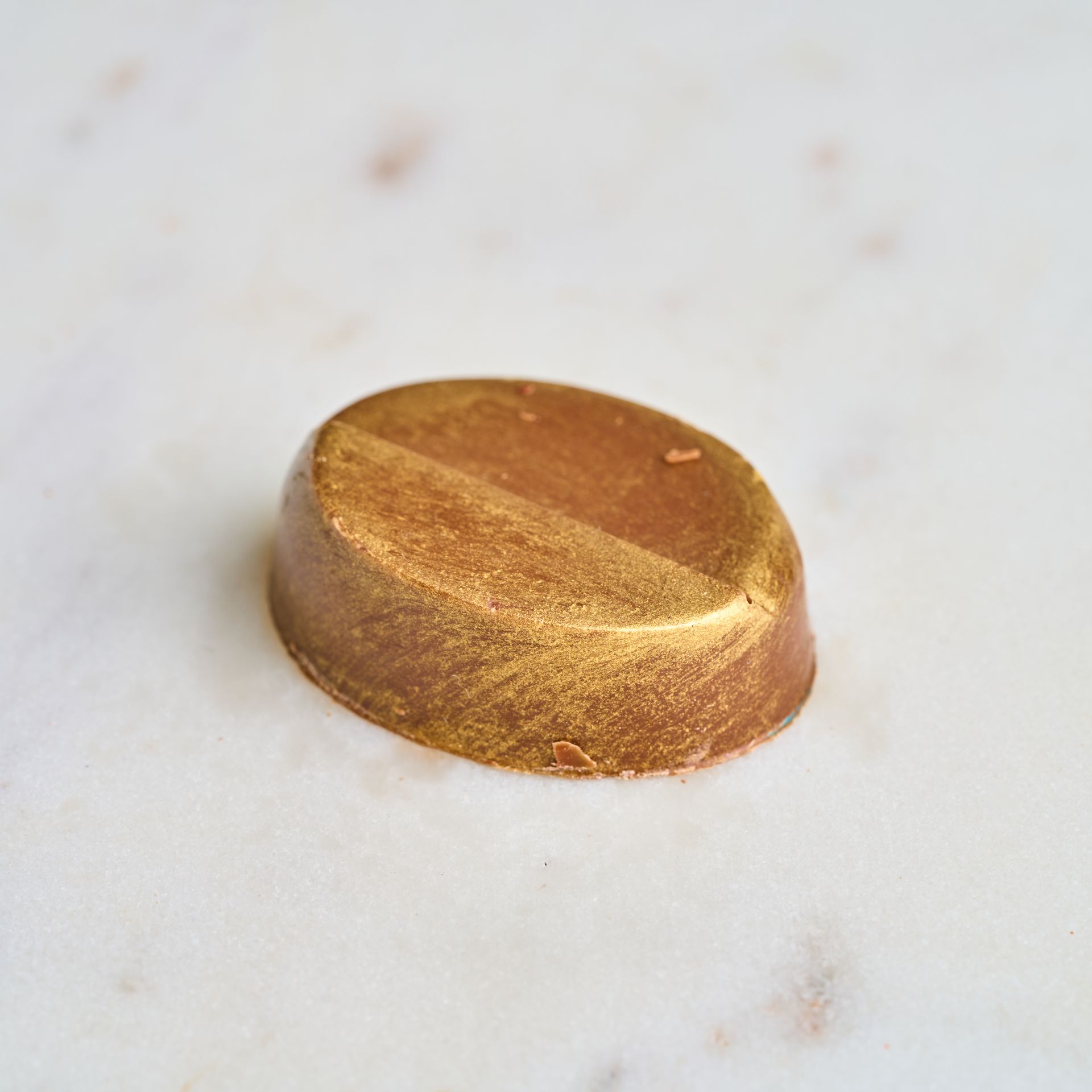 Golden-brown oval-shaped chocolate, half-divided, on a marble surface.