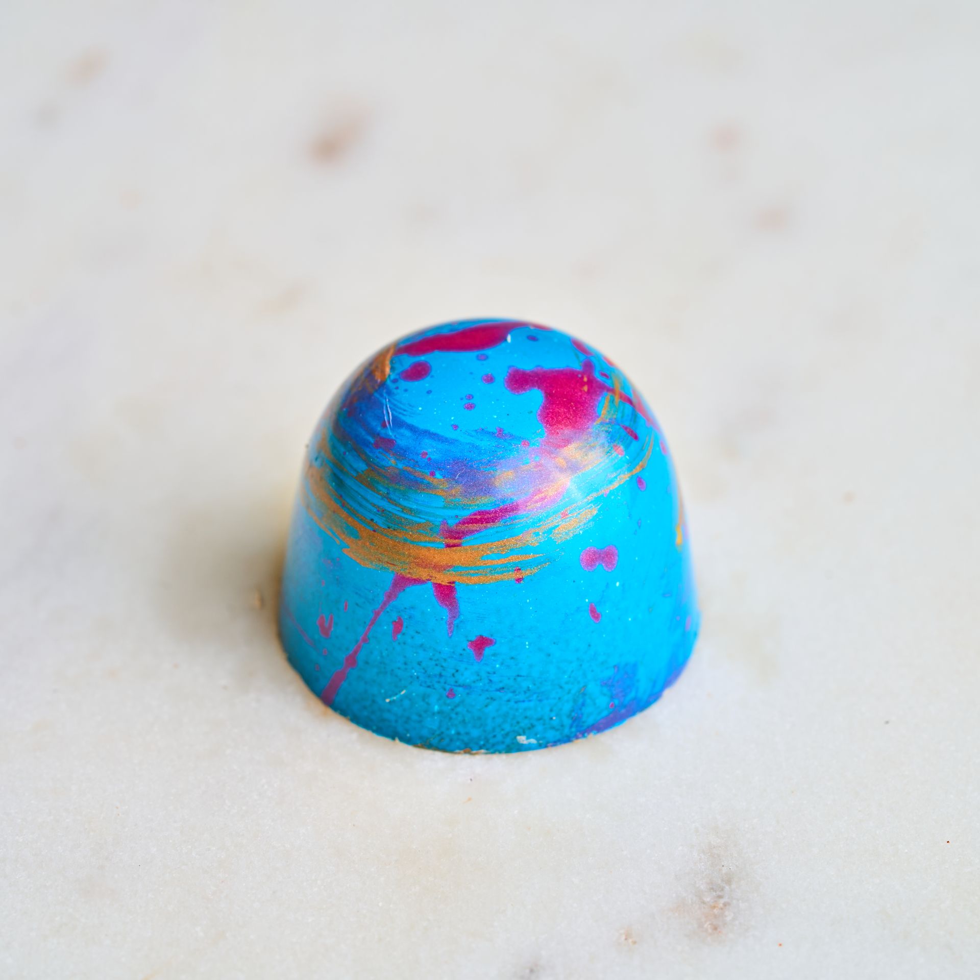 Blue chocolate truffle with pink and gold paint splatters.