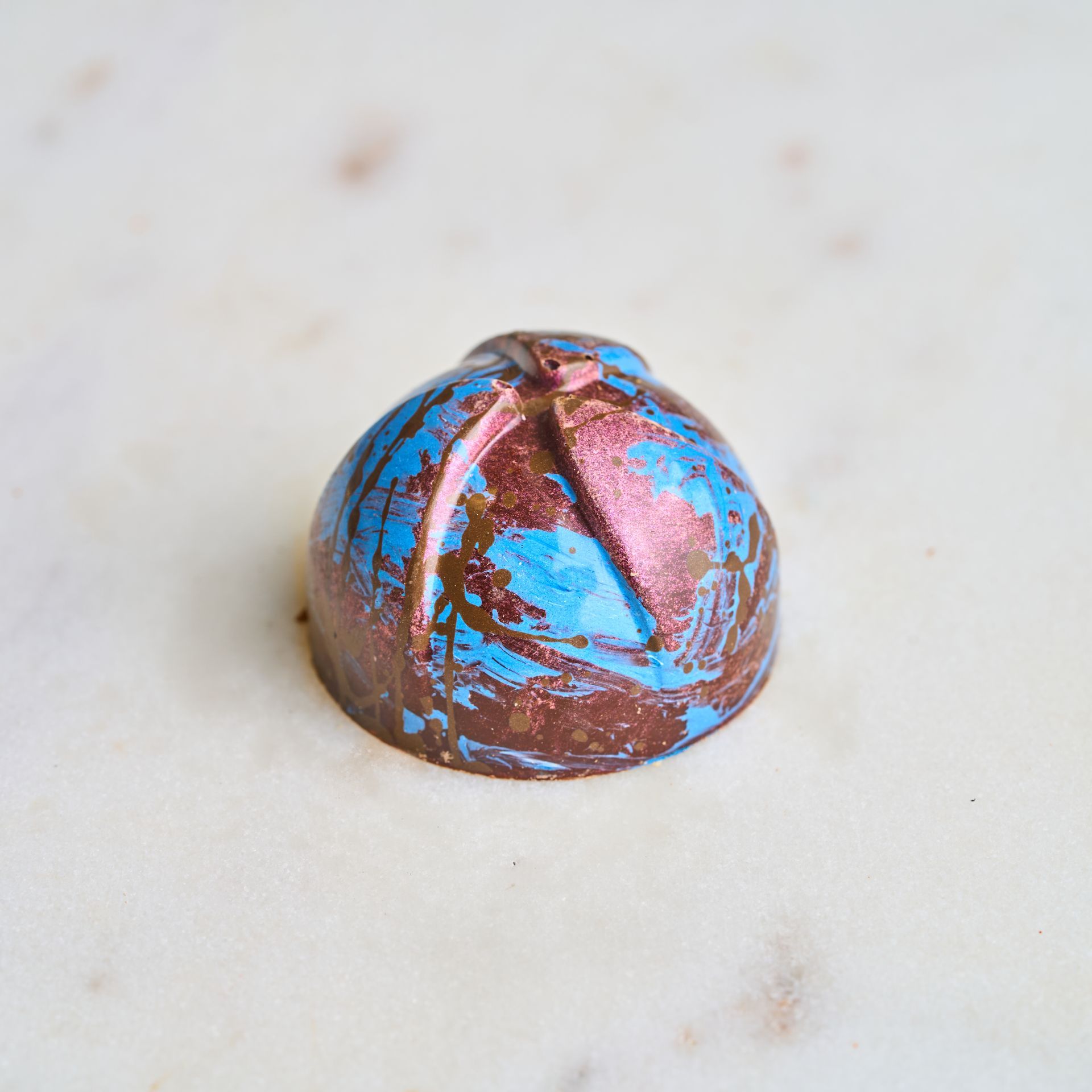 Chocolate truffle with blue and bronze colored swirls on white surface.