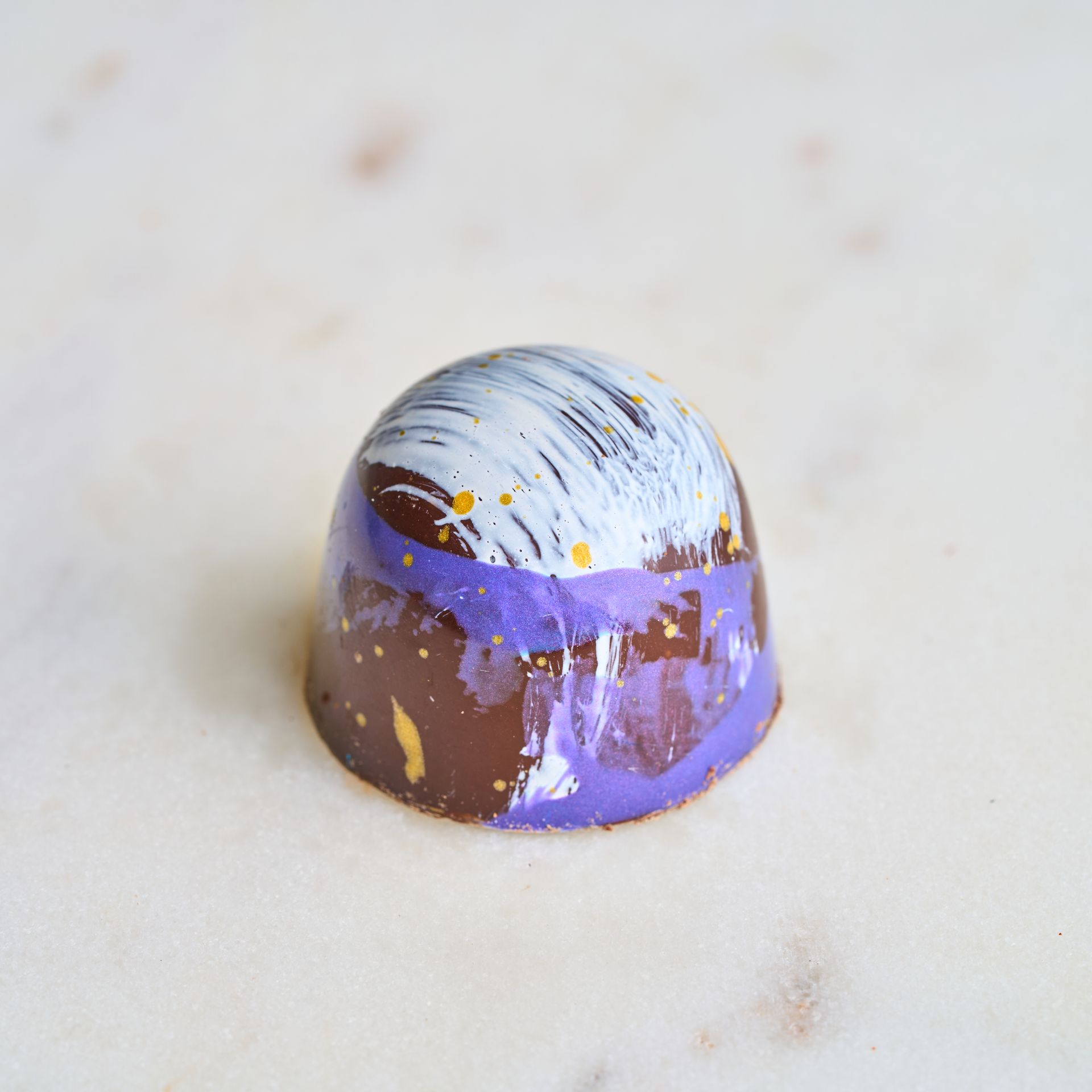 Chocolate truffle with purple, white, and gold accents on a marble surface.