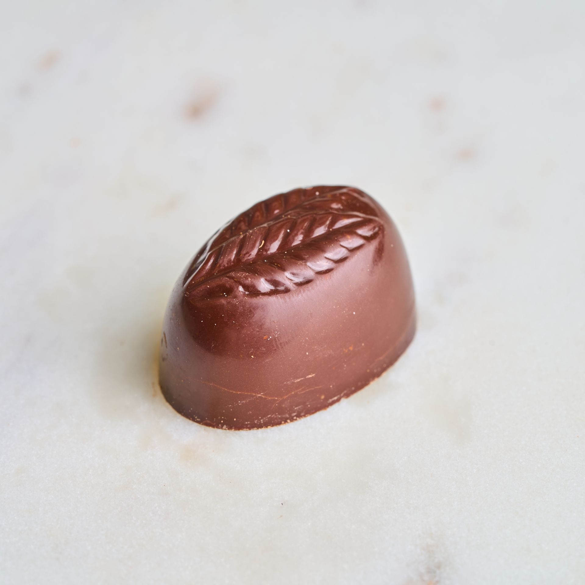 Chocolate candy with a leaf design on a marble surface.