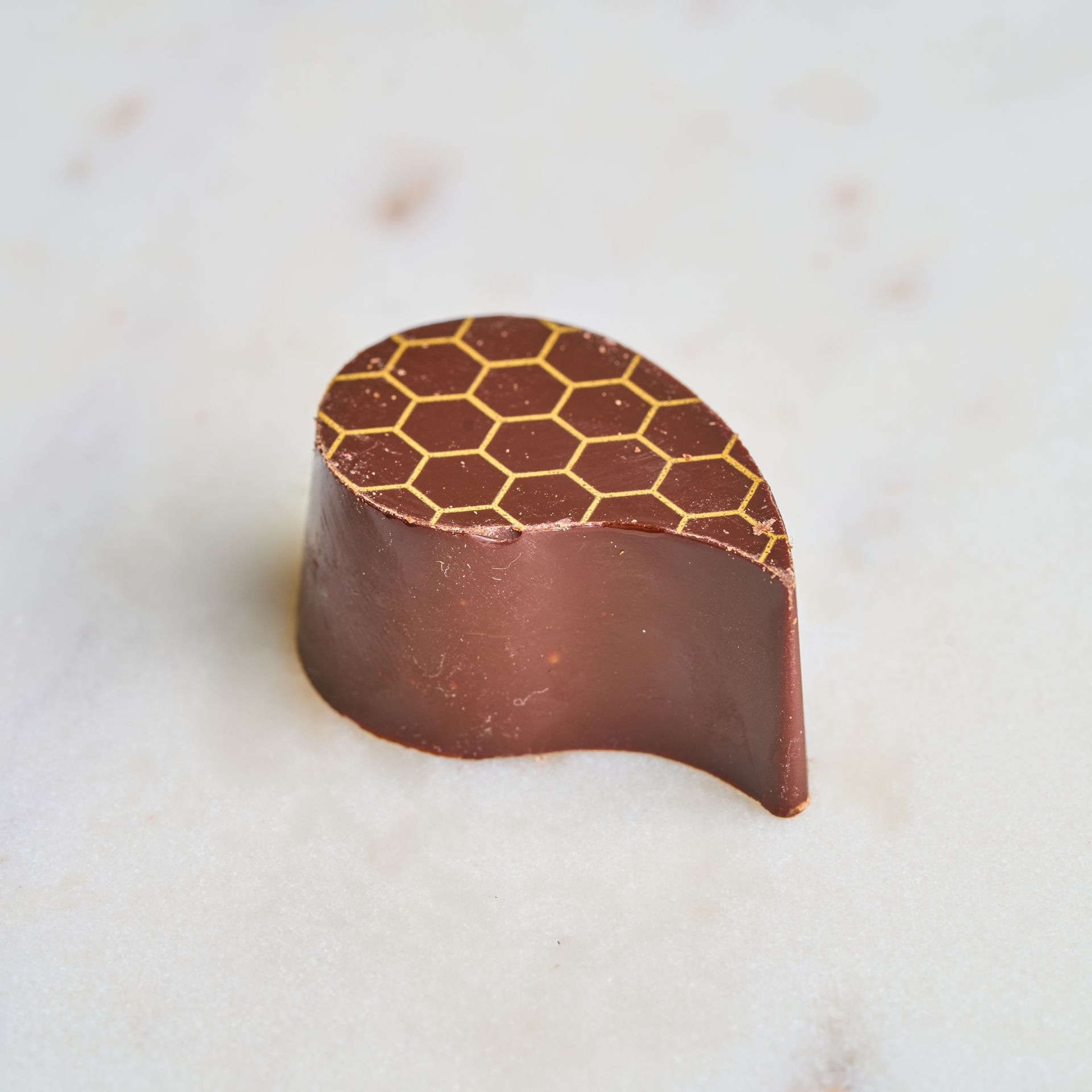 Dark chocolate candy, teardrop shape, with honeycomb pattern on top, set on marble.
