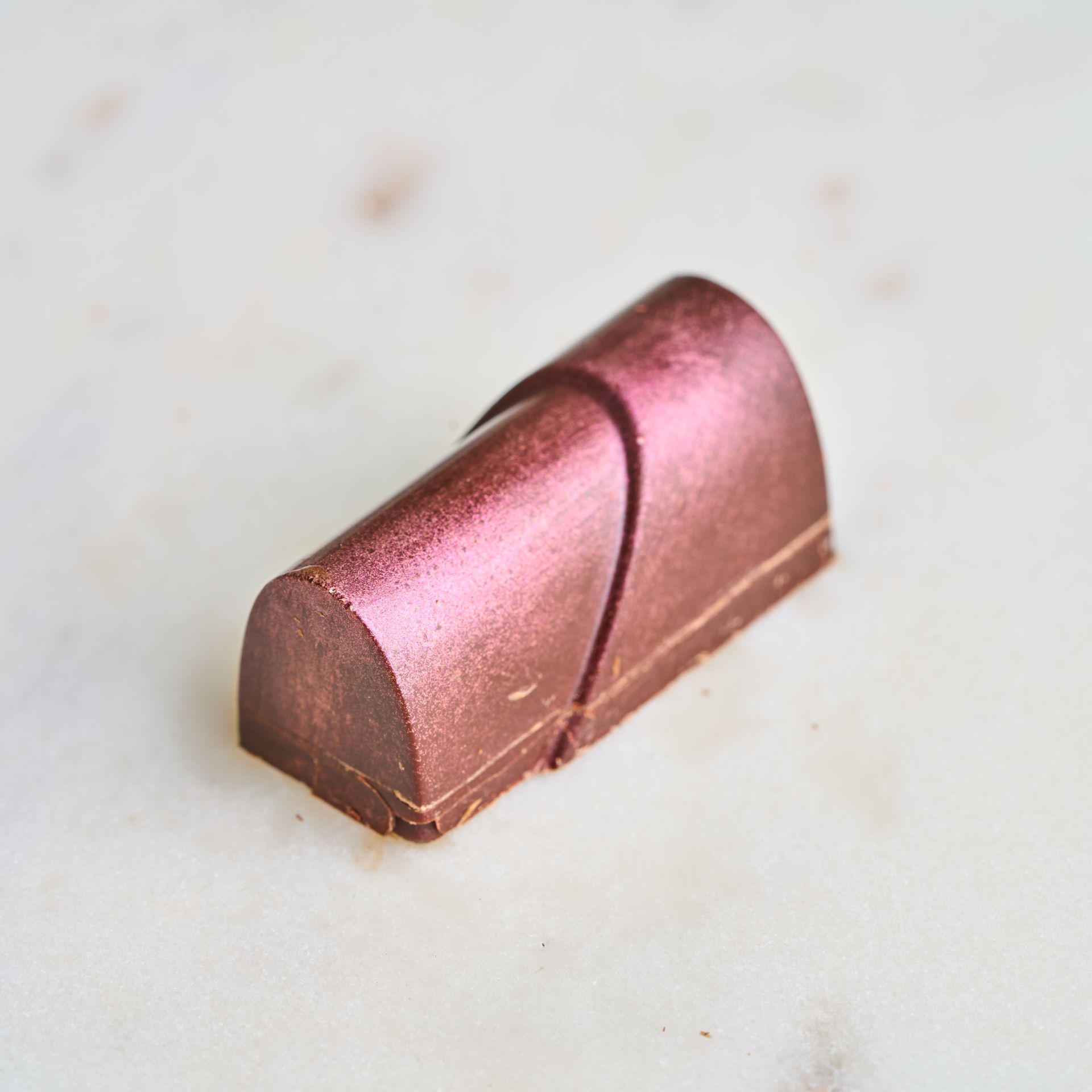 Chocolate candy, half-cylinder shape, dark pink with diagonal line, on marble surface.