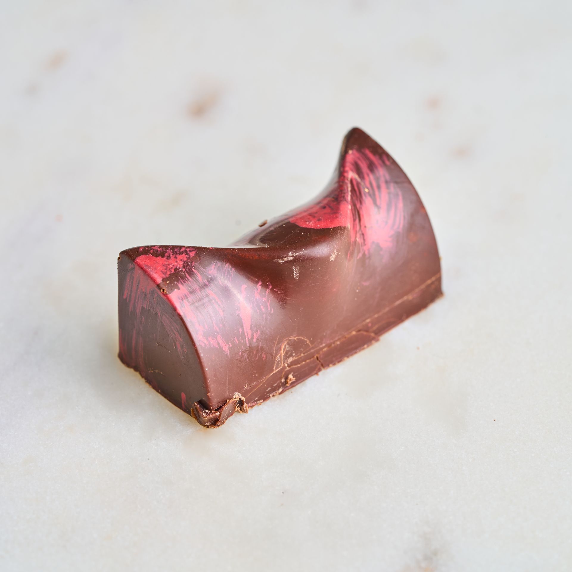 Chocolate candy with pink streaks on a white marble surface.
