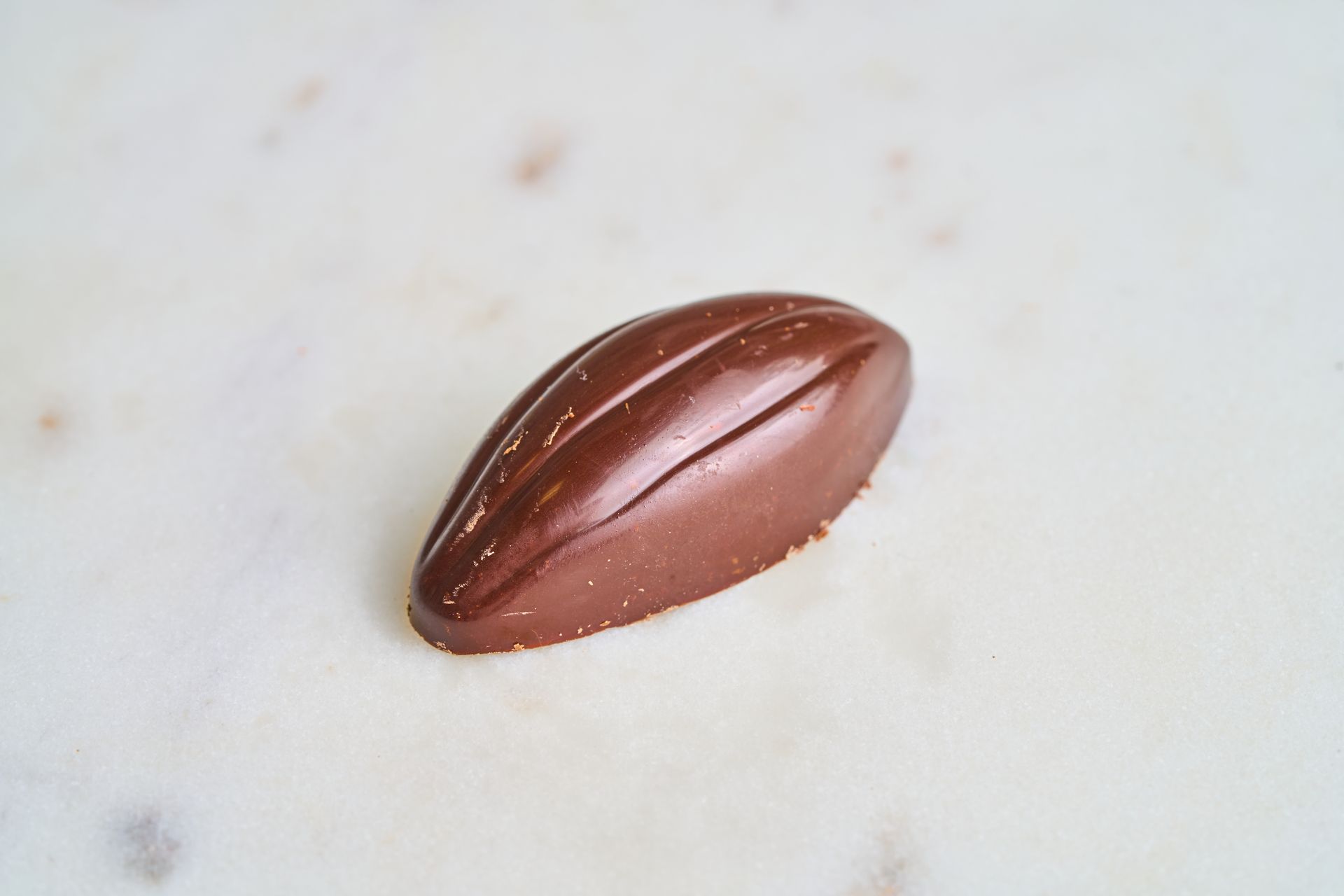Chocolate candy in the shape of a cacao bean, on a white marble surface.