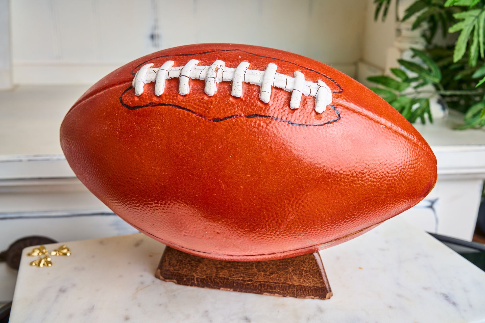 Brown football, with white laces, on a brown pedestal, sits on a white marble surface.