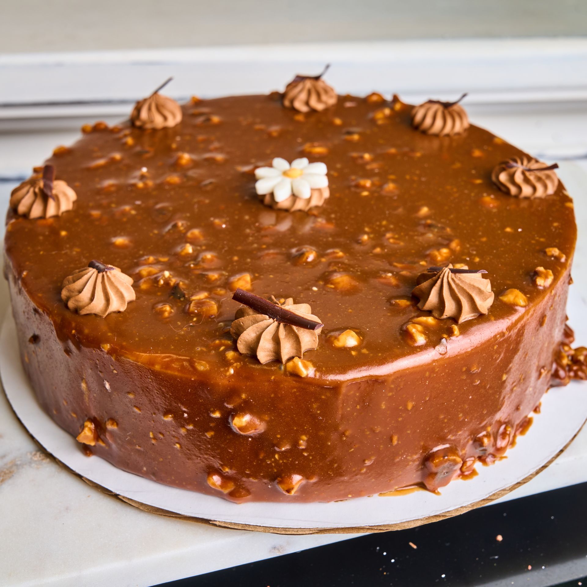 Round caramel cake with nut topping and cream decorations.