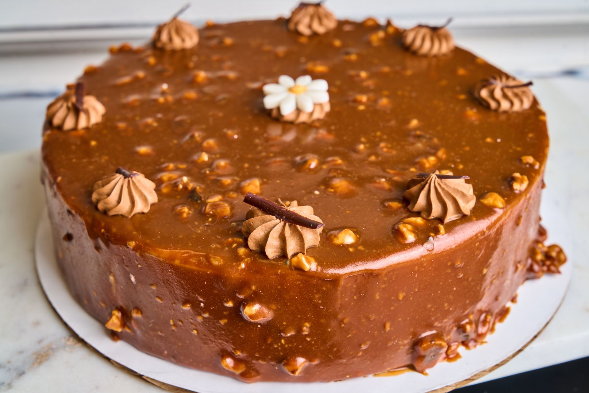 Chocolate cake with caramel glaze, nuts, and piped frosting.