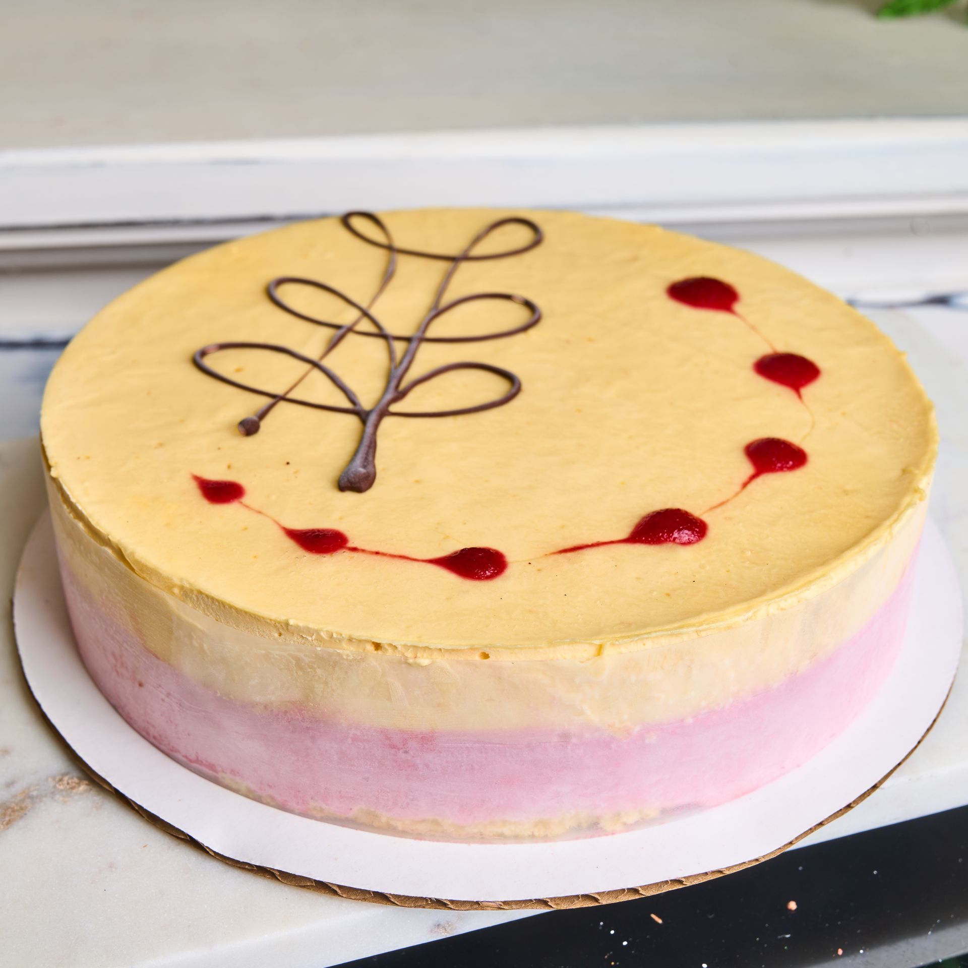 Cake with a yellow top layer, pink bottom, and chocolate swirl design with red dots.