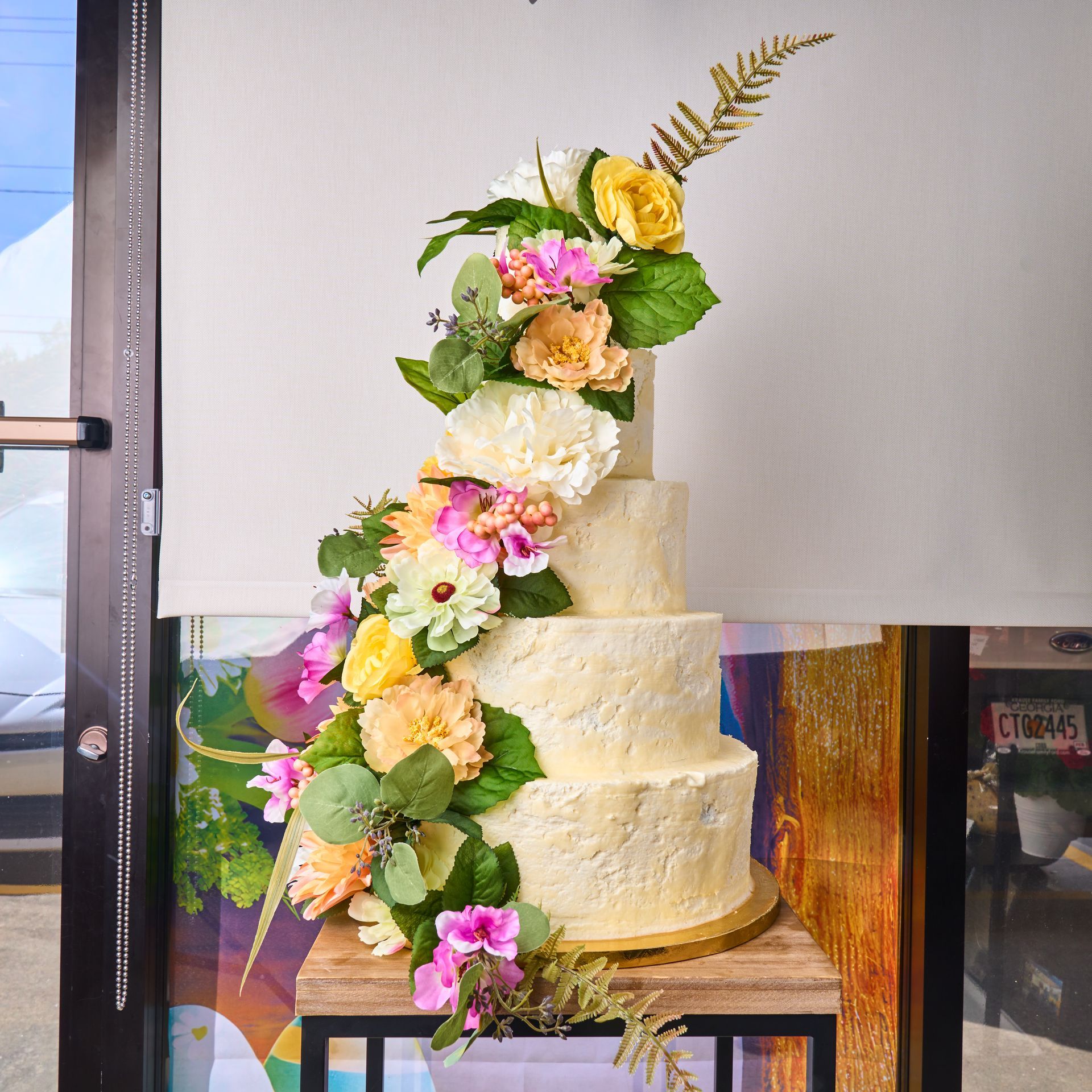 Four-tiered cake decorated with cascading flowers in yellow, pink, and peach, on a wooden stand.