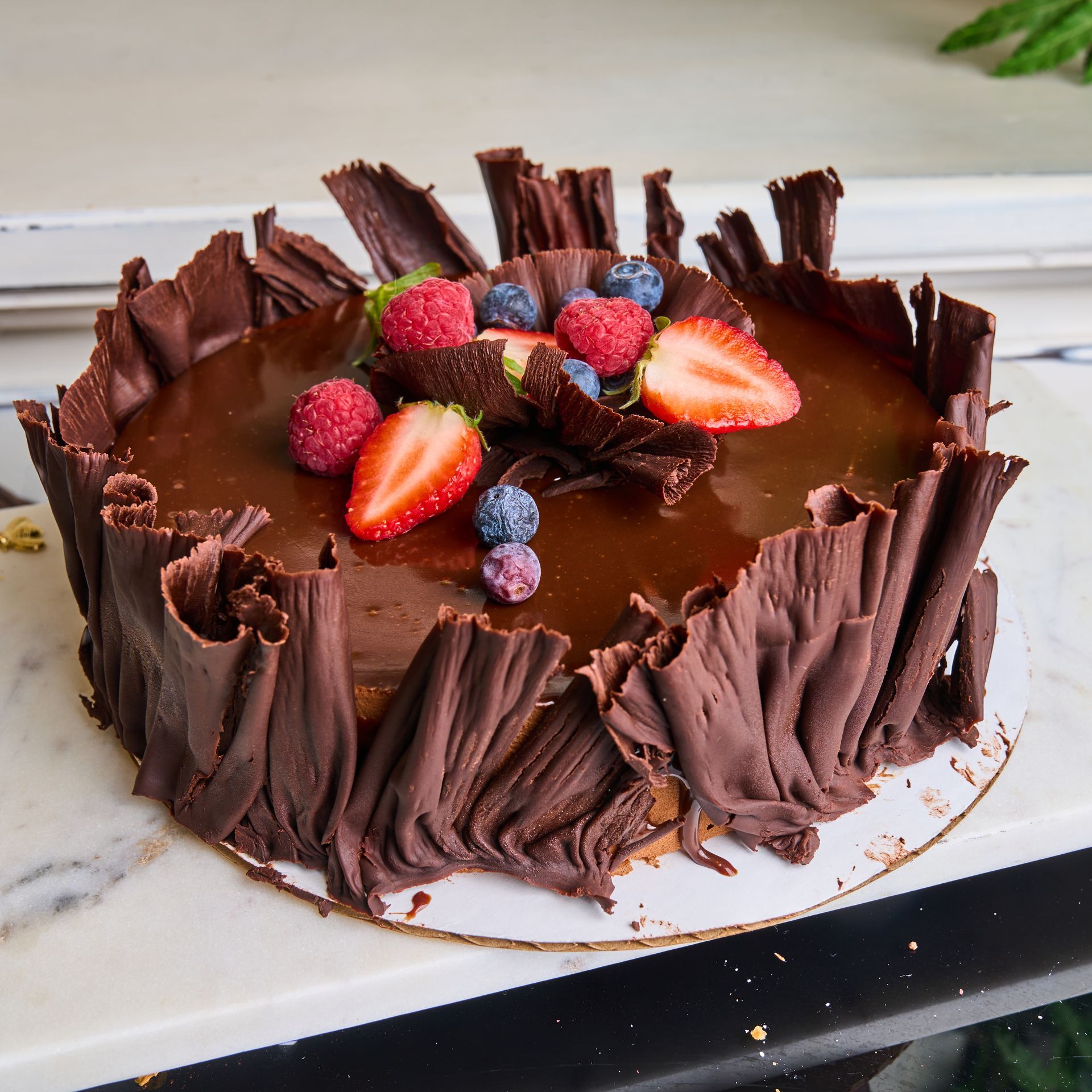 Chocolate cake with glaze and chocolate shavings, topped with berries.