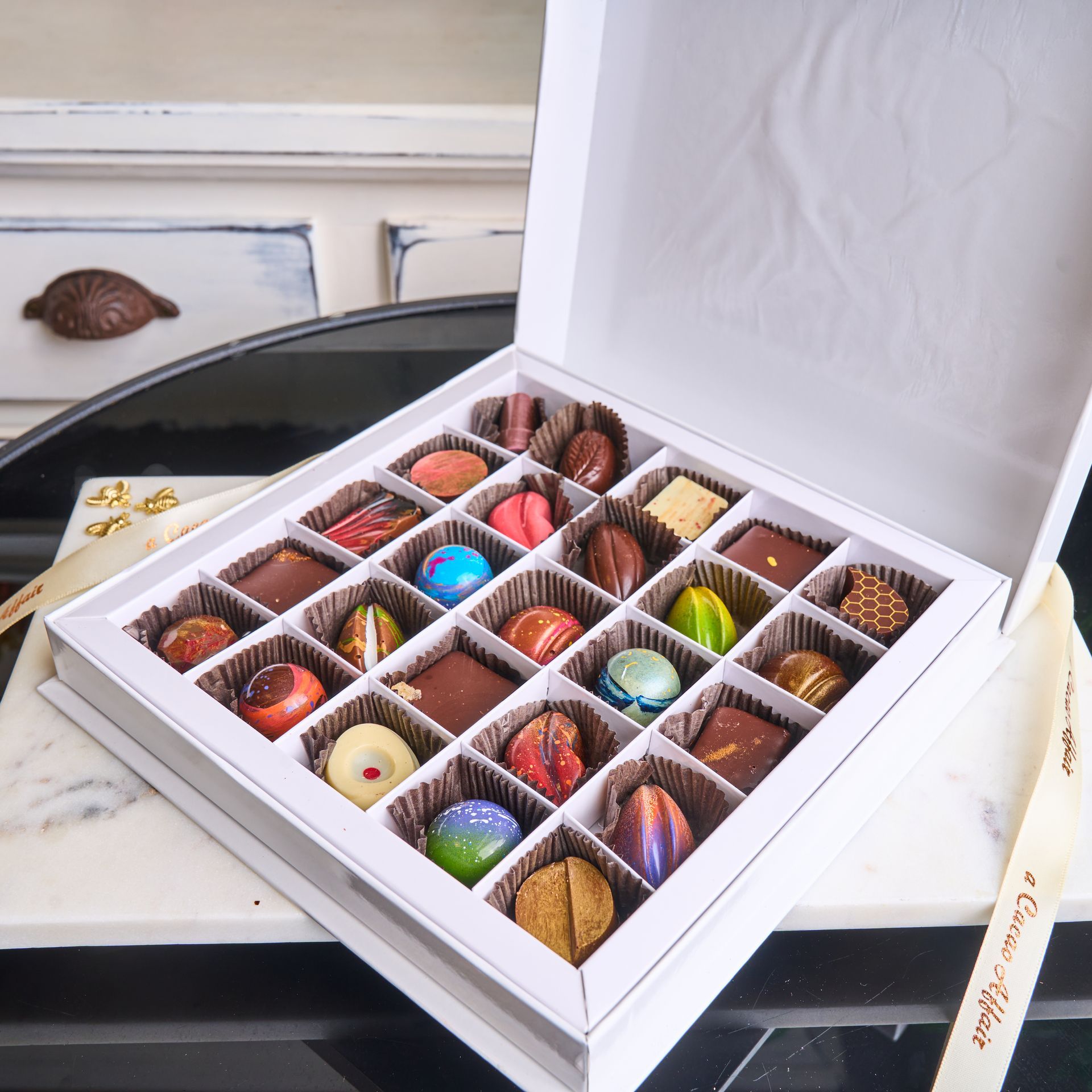 Box of assorted colorful chocolates, open on a marble surface.