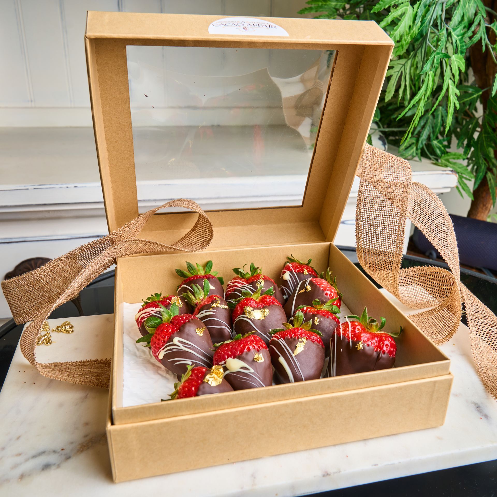 Chocolate-covered strawberries in a gift box with a ribbon. The box has a clear lid, and the strawberries are decorated with white chocolate.