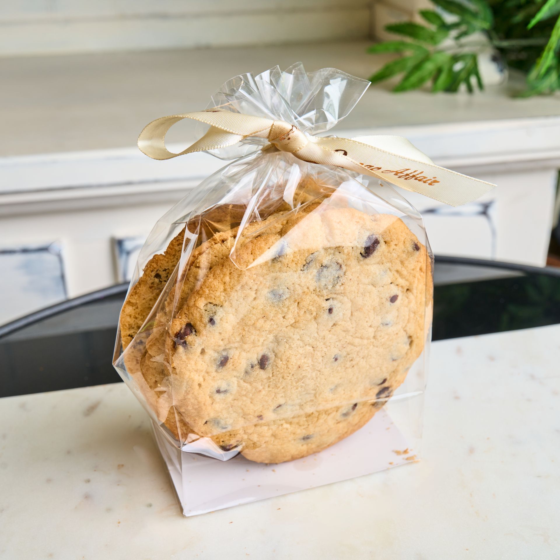 Chocolate chip cookies in clear cellophane bag, tied with beige ribbon.