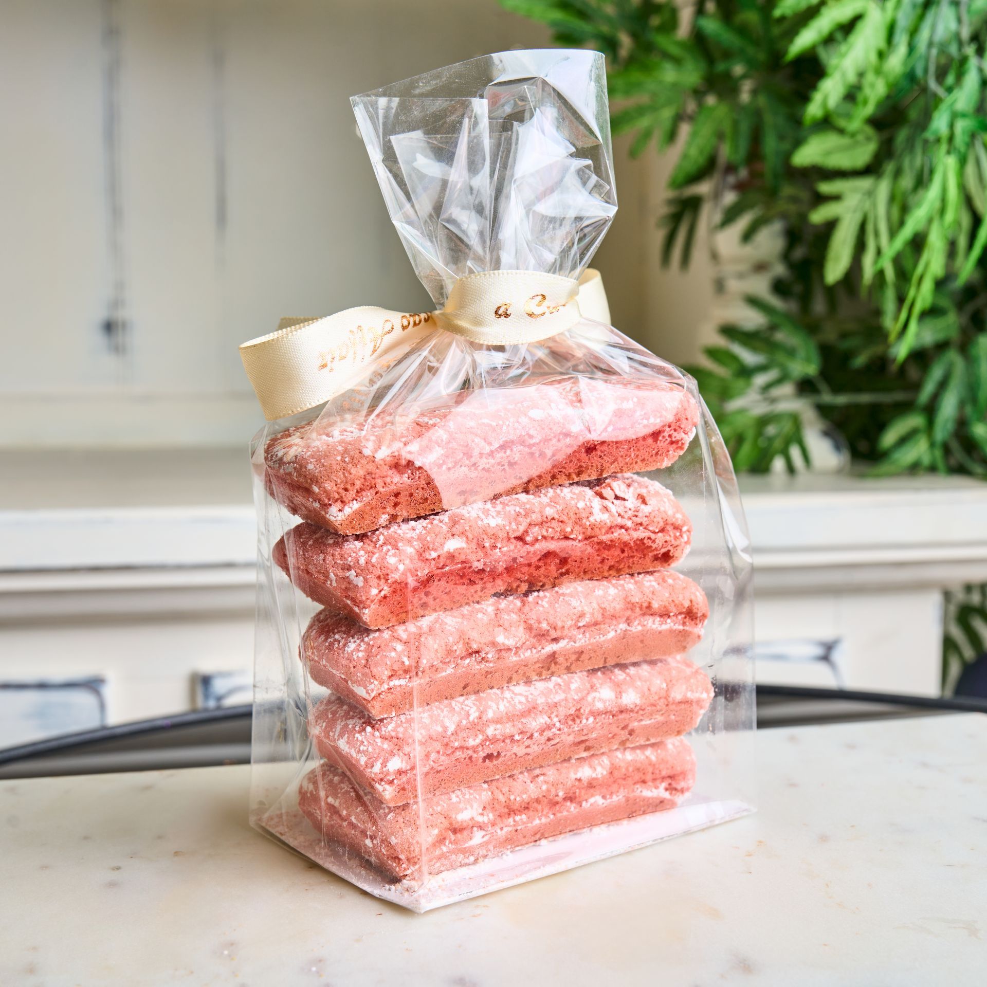Bag of pink cookies tied with a beige ribbon on a white tabletop.