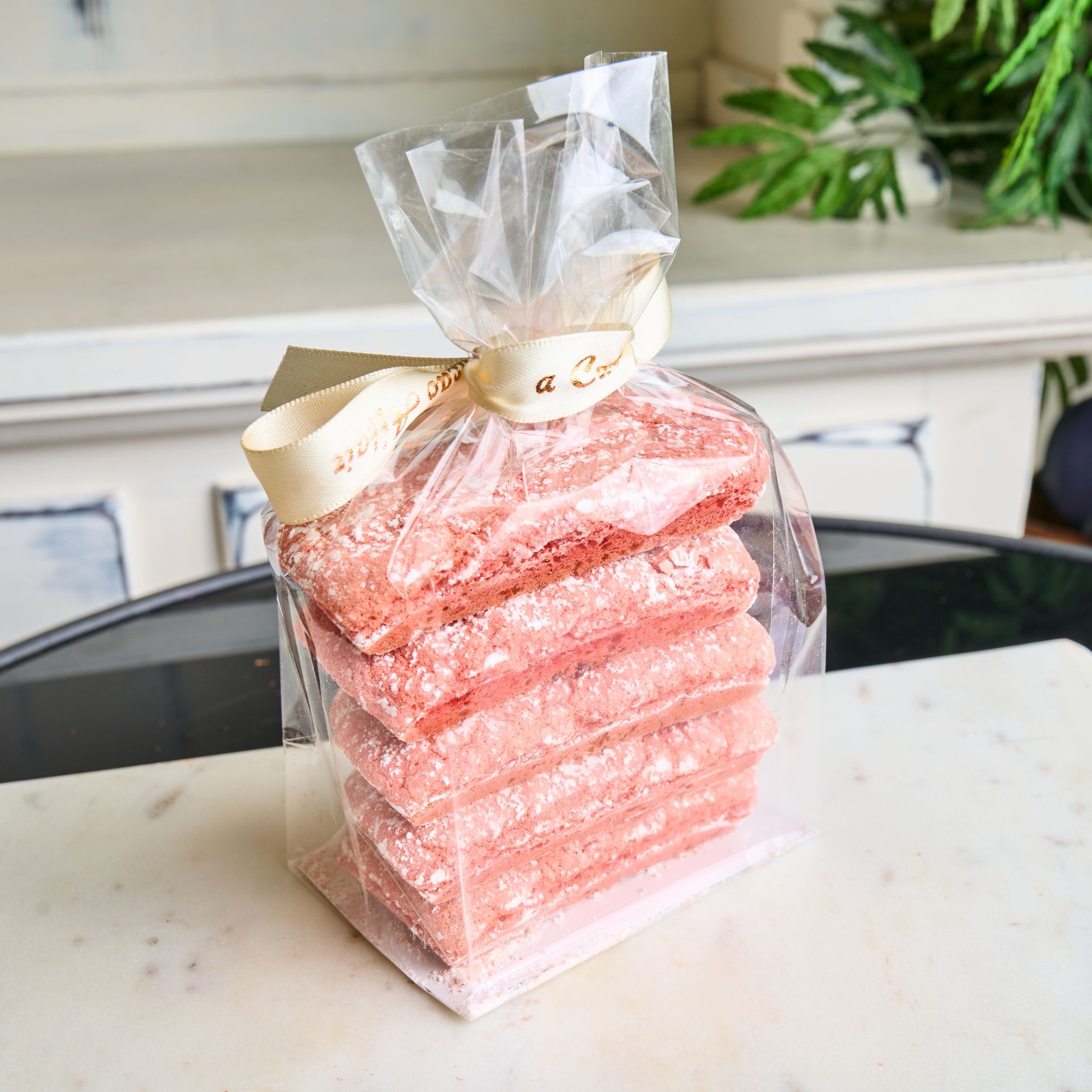 Stack of pink cookies in a clear bag, tied with a cream-colored ribbon, on a marble surface.