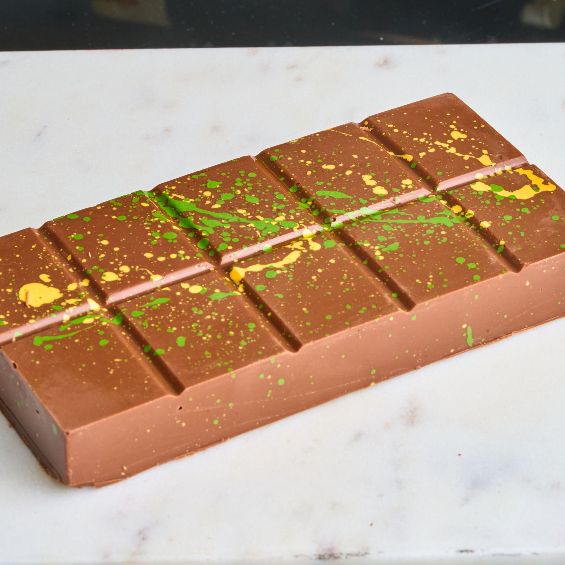 Chocolate bar with green and yellow splatters on a white surface.